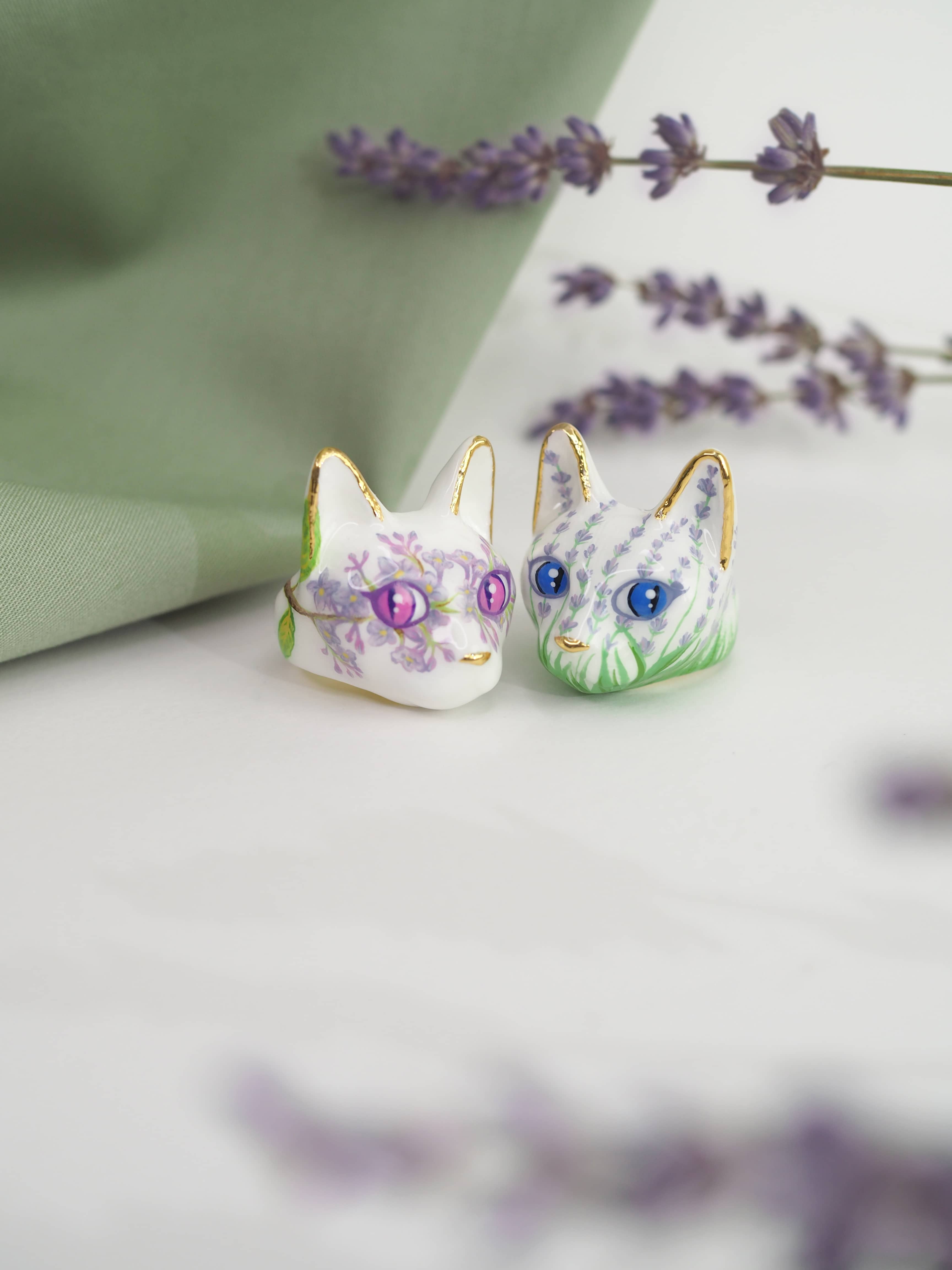 Two unique cat rings with colorful floral patterns placed against a soft green background, alongside sprigs of lavender.