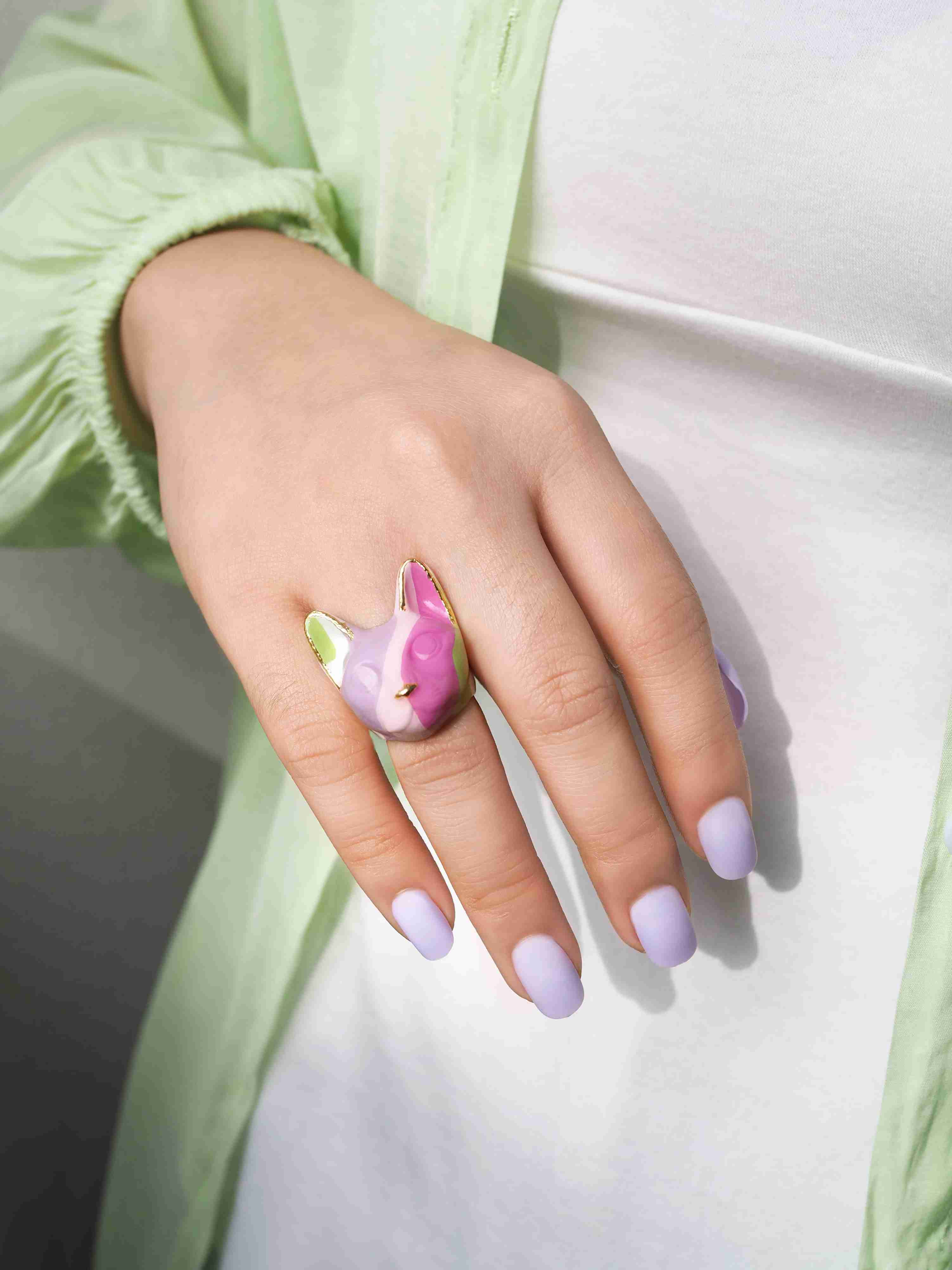 Close up of a hand adorned with unique cat ring in purple, pink, green, and white, with a casual outfit.