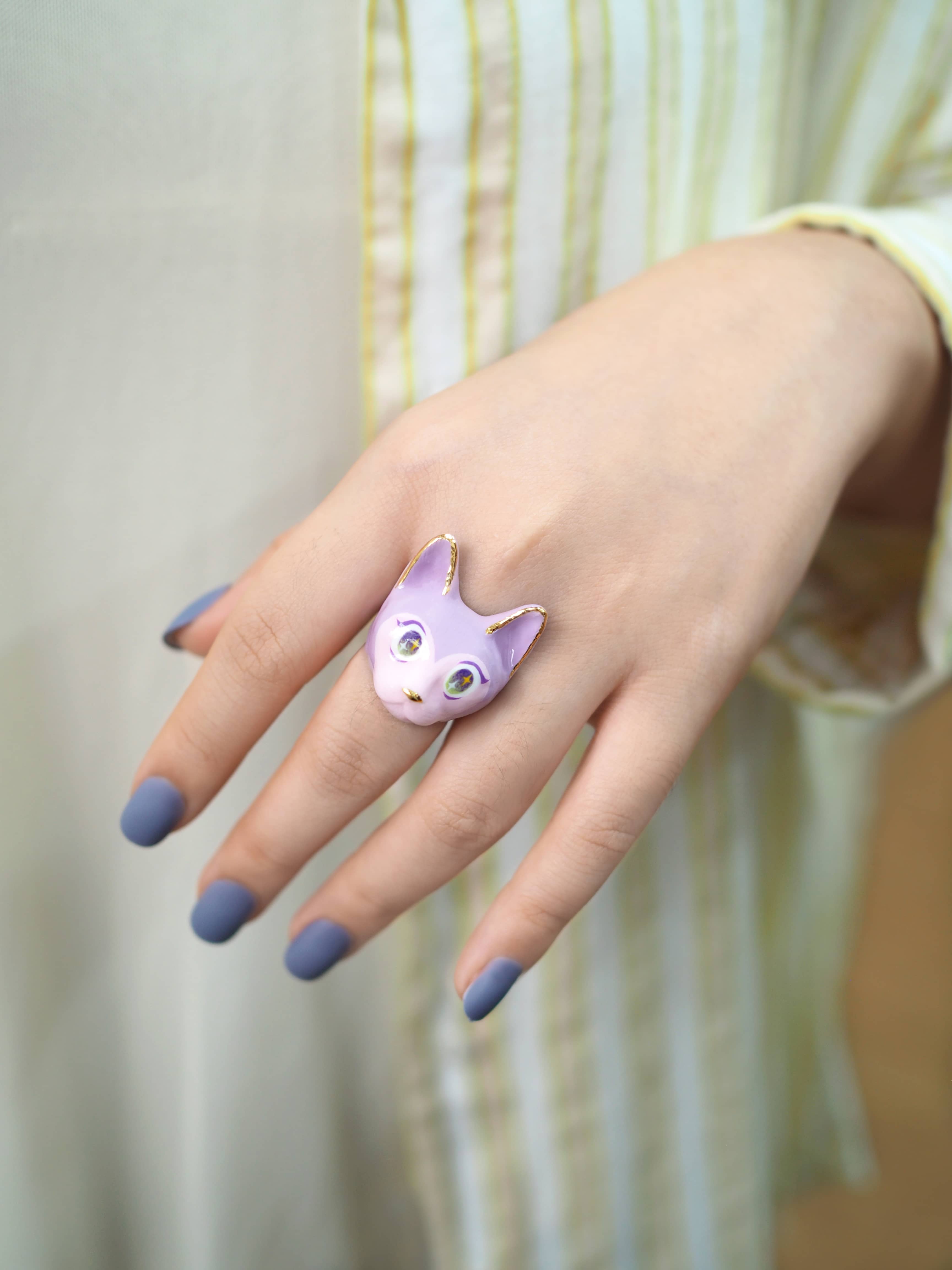 A hand with lavender nails wears a cute purple cat ring.