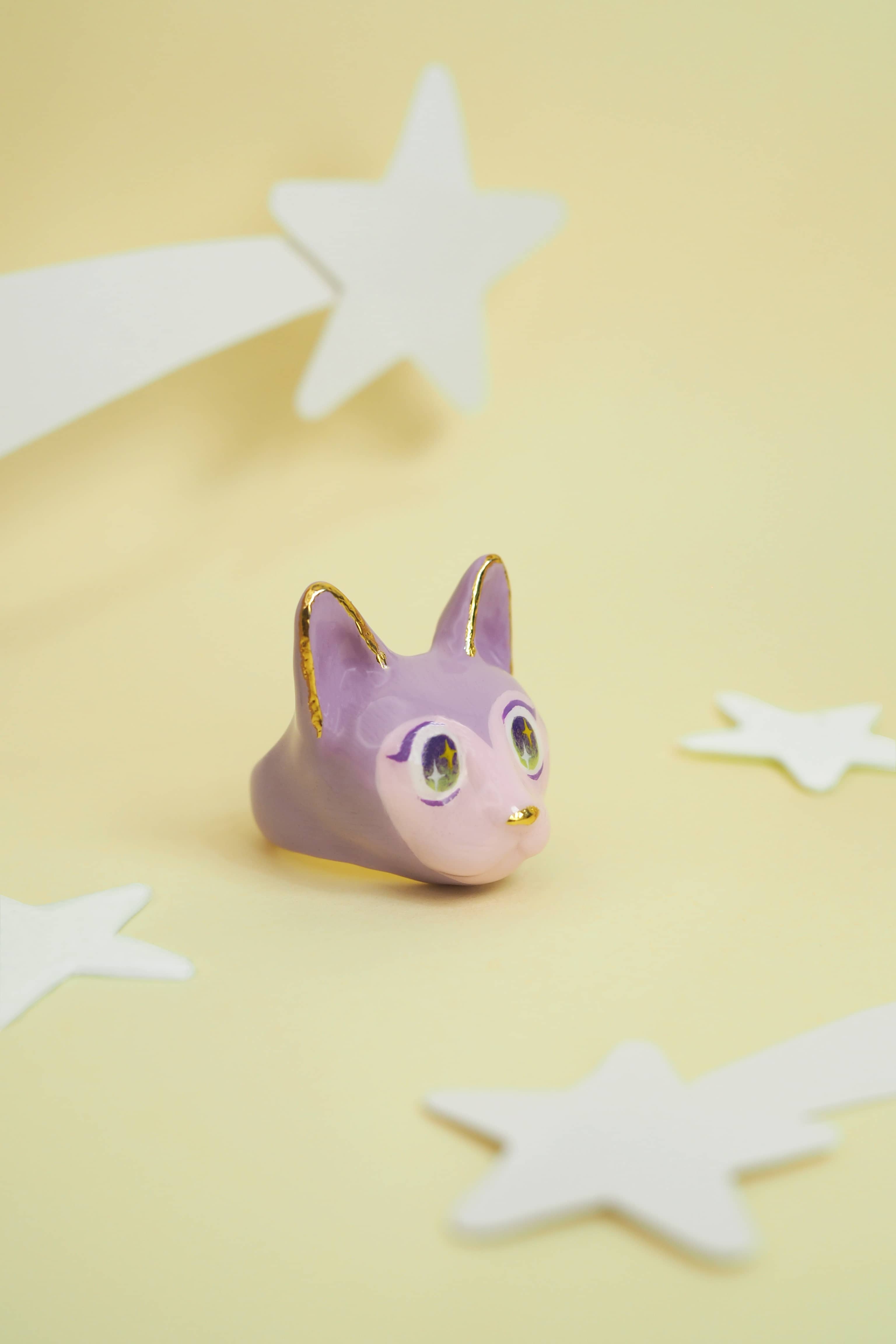 A playful cat rings in purple and pink, each with big eyes placed on a soft yellow background with stars.