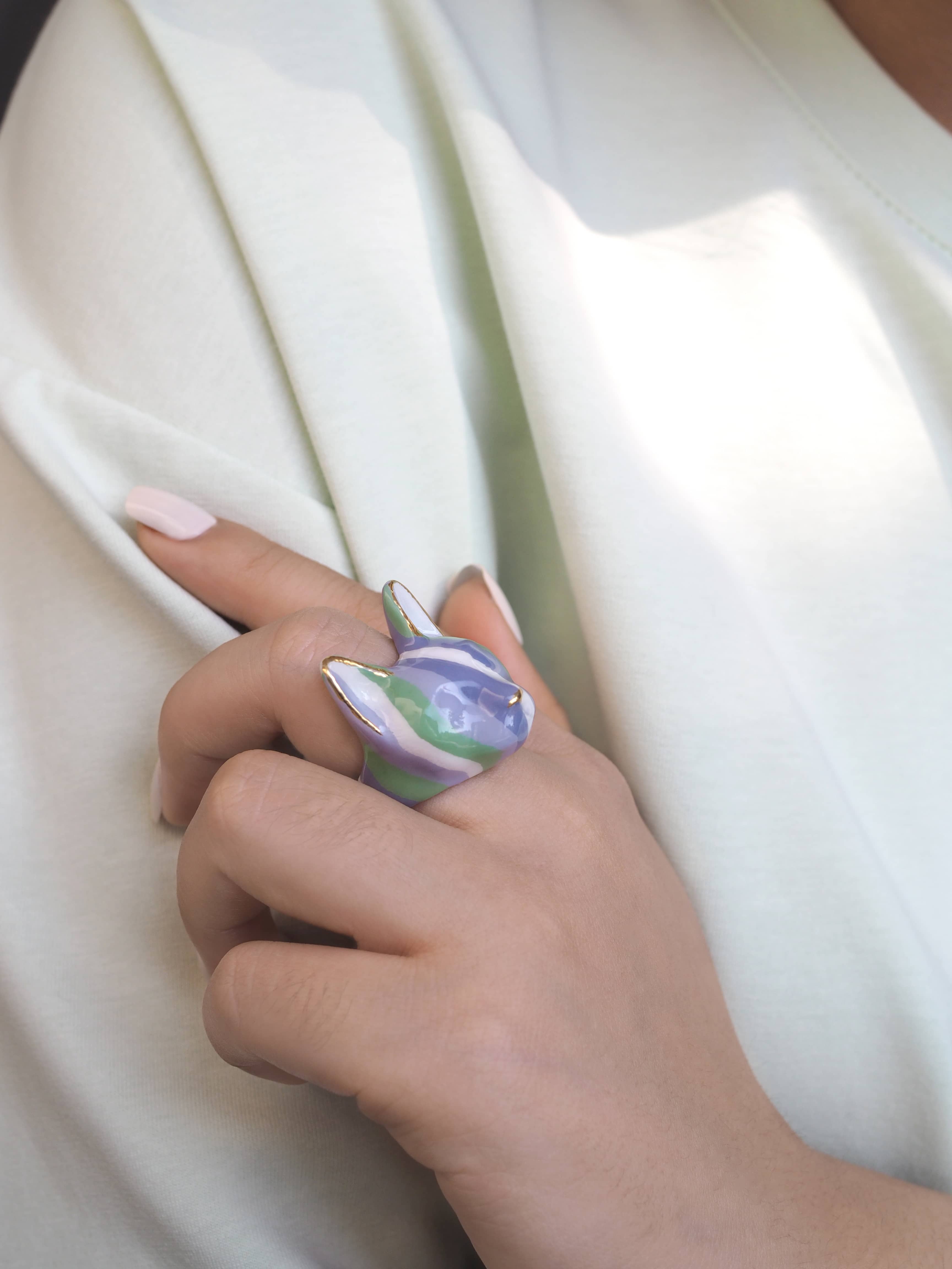 Close-up of a hand wearing a cat ring designed with stripes of green and purple.