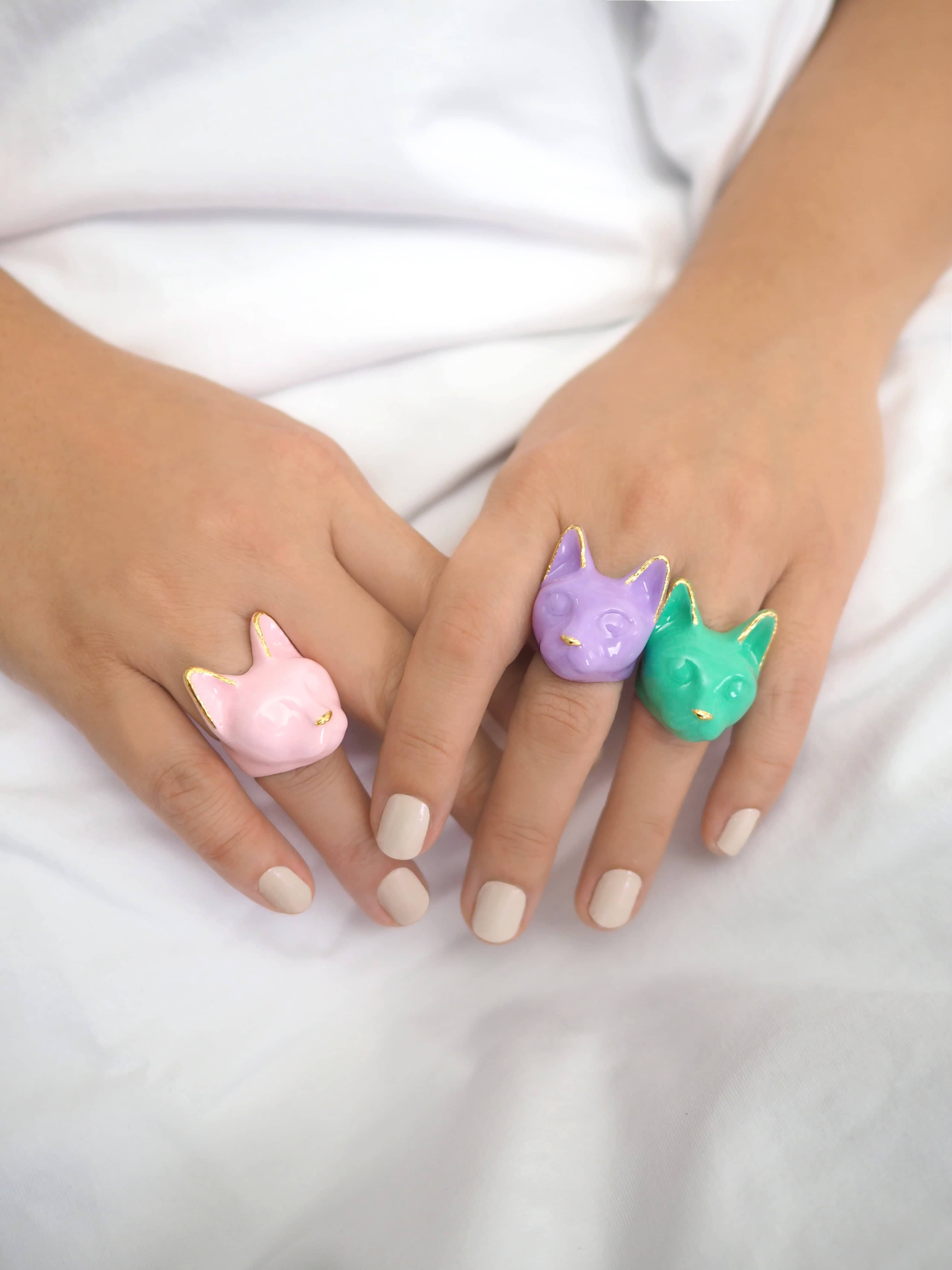 Three colorful cute cat rings in pink, purple, and green on a woman's hands