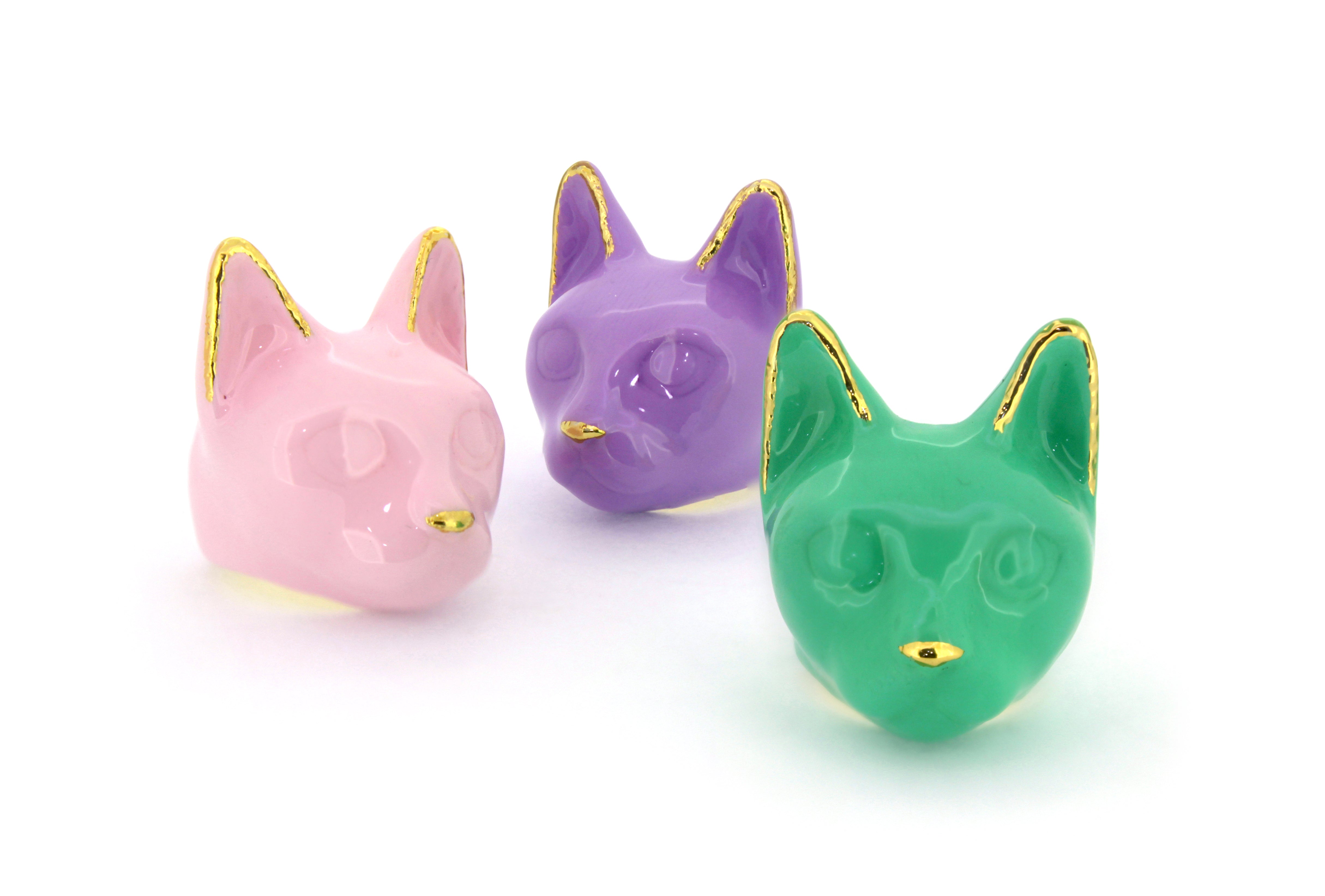 Three cat heads ring in pastel colors—pink, purple, and green—each with gold accents on ears and nose.