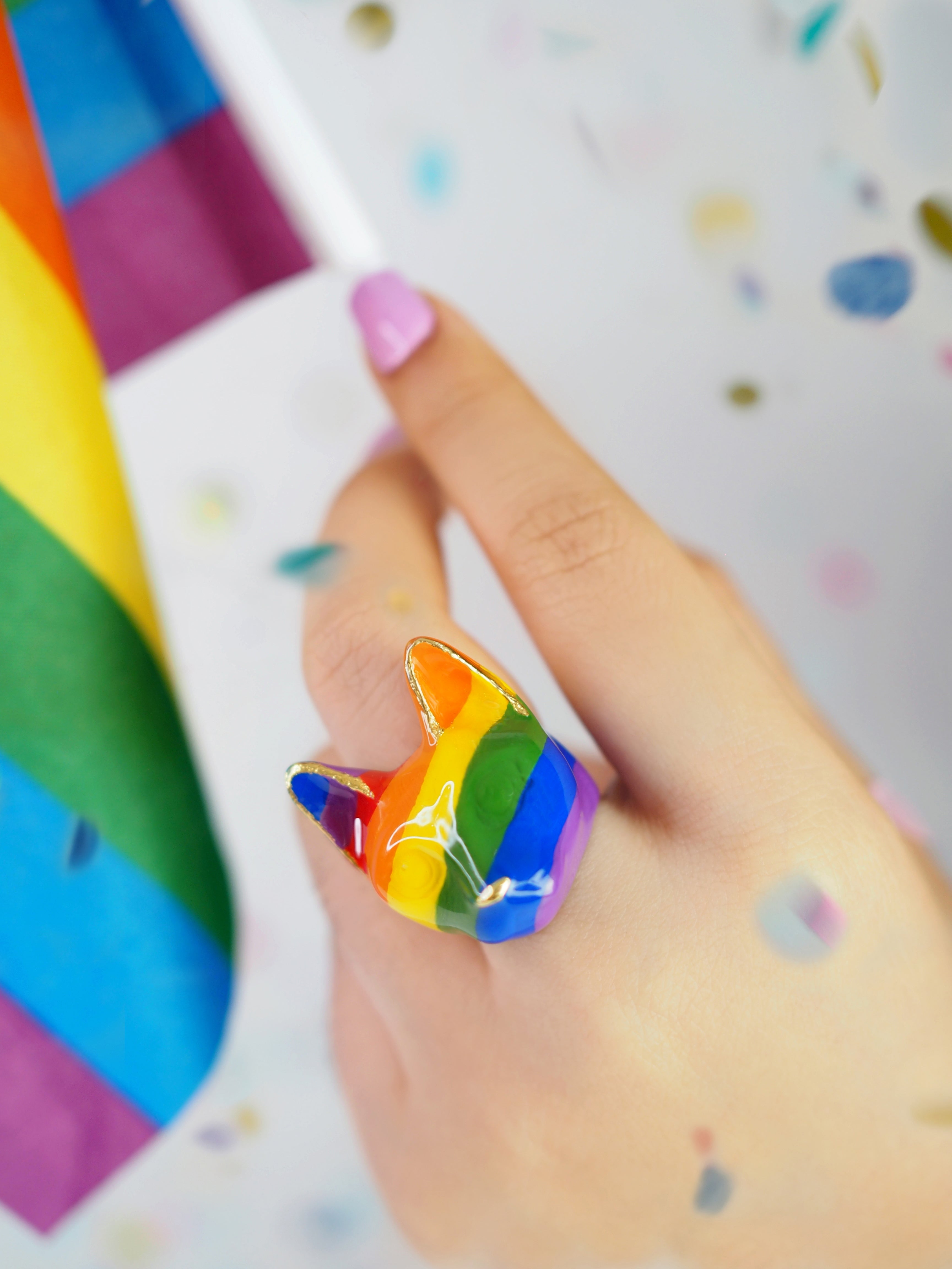 Close-up of a hand wearing a cat ring showcasing stripes with vibrant rainbow stripes while holding a Pride flag.