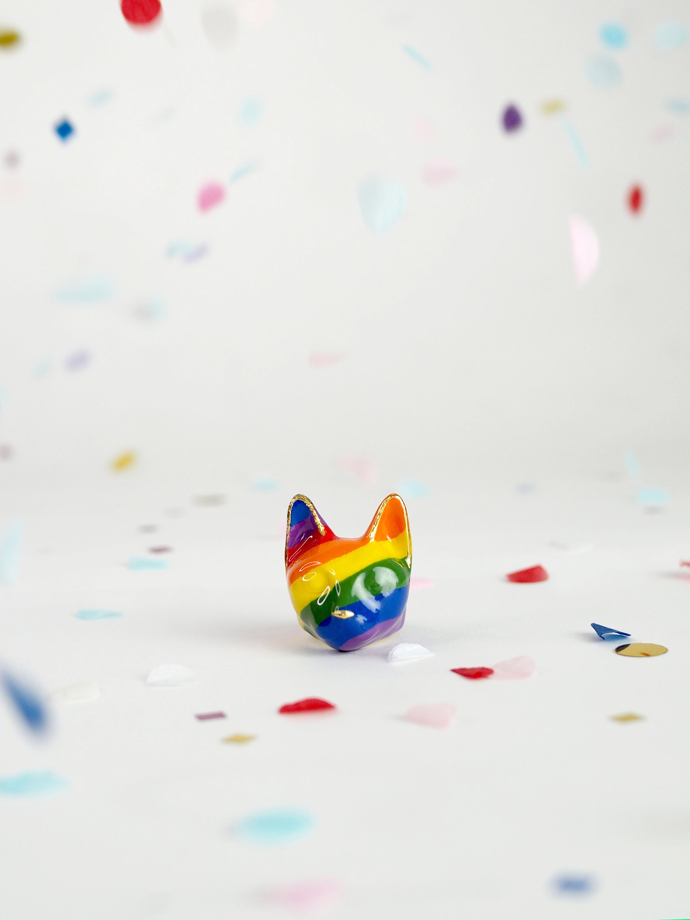 Colorful rainbow cat ring surrounded by confetti on a light background, celebrating Pride Month.