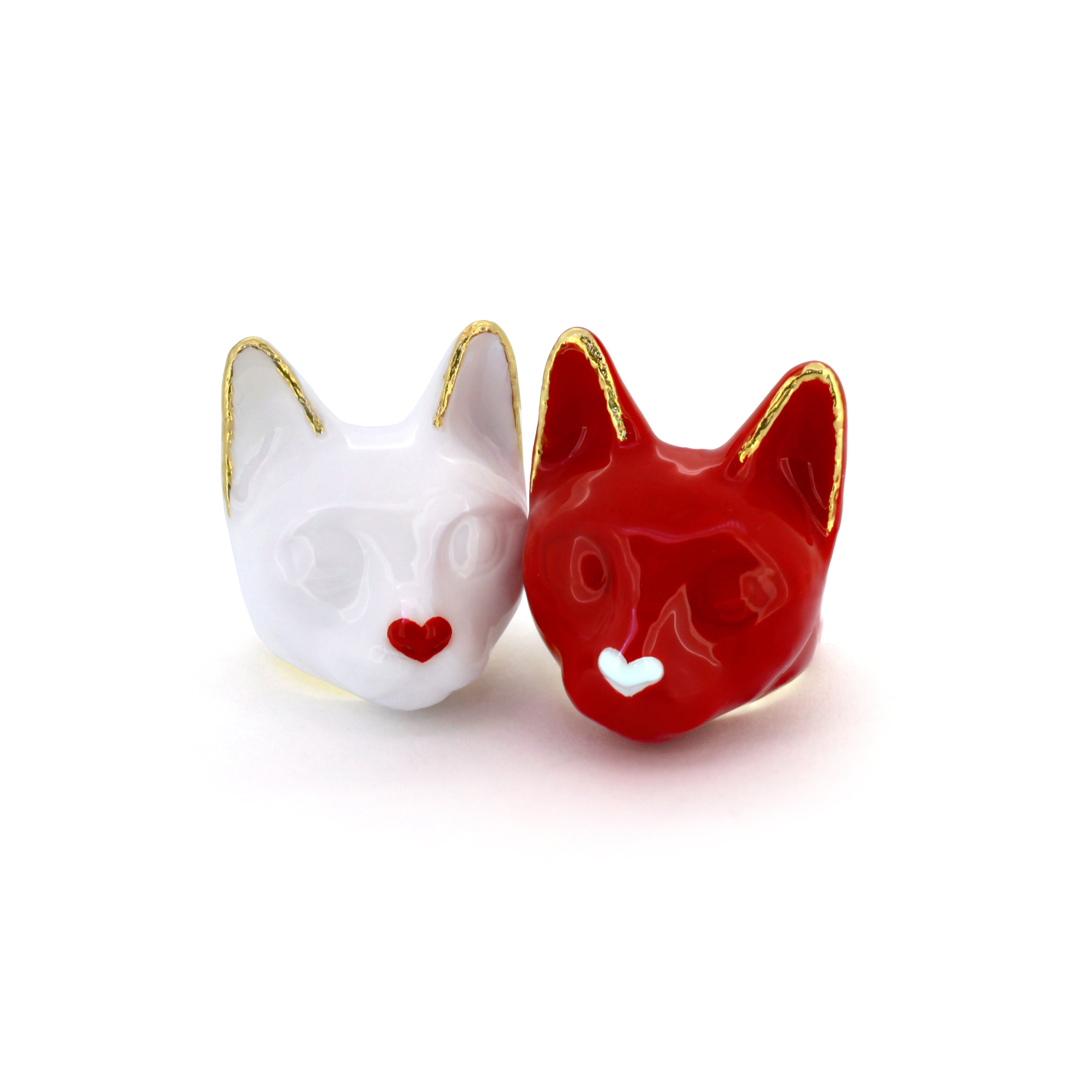 Two cat rings, one white with a small red heart-shaped nose other red with a small white heart-shaped nose.