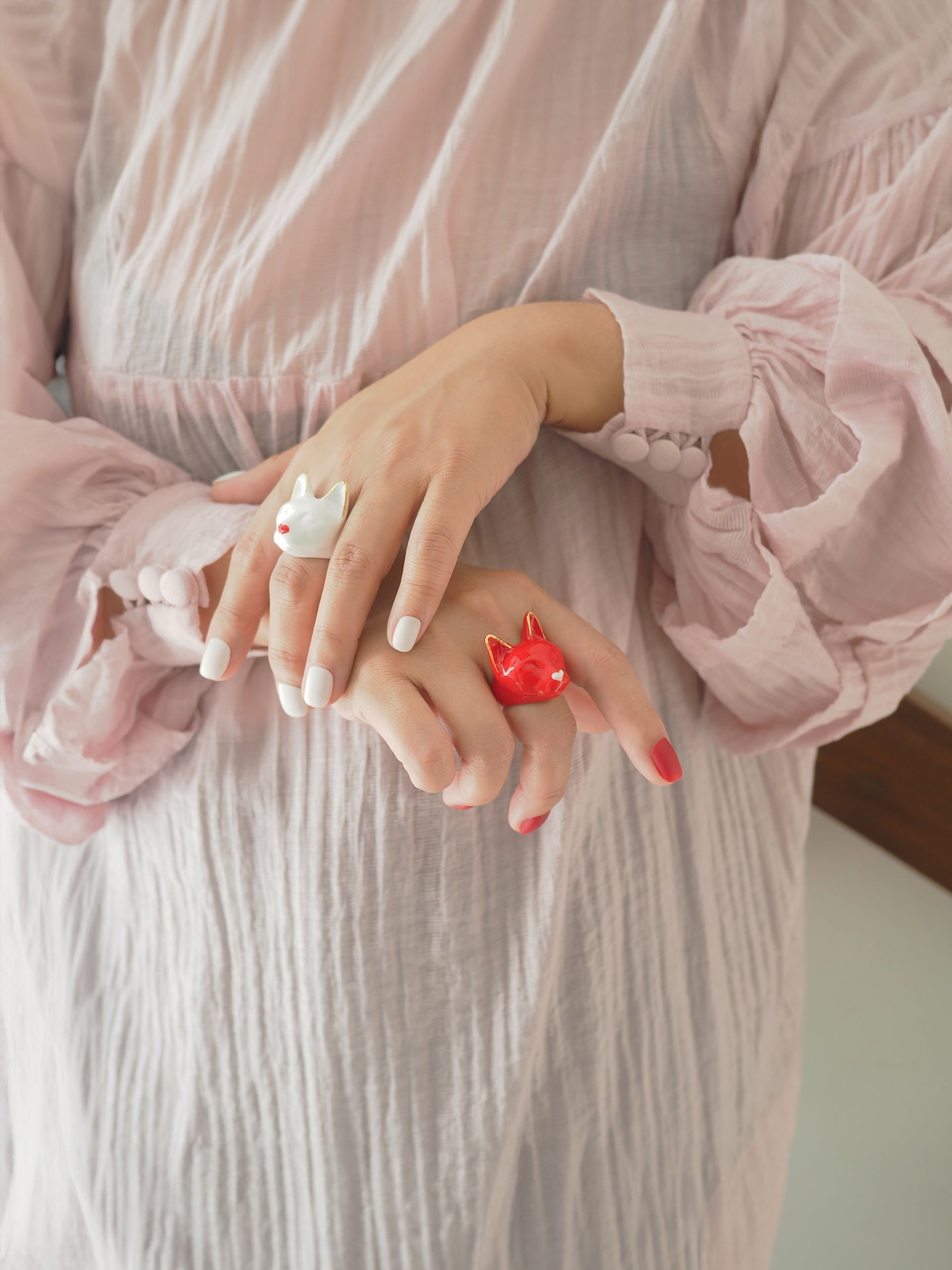 Two colorful cat rings in red and white on a person's hands, wearing a light pink dress.