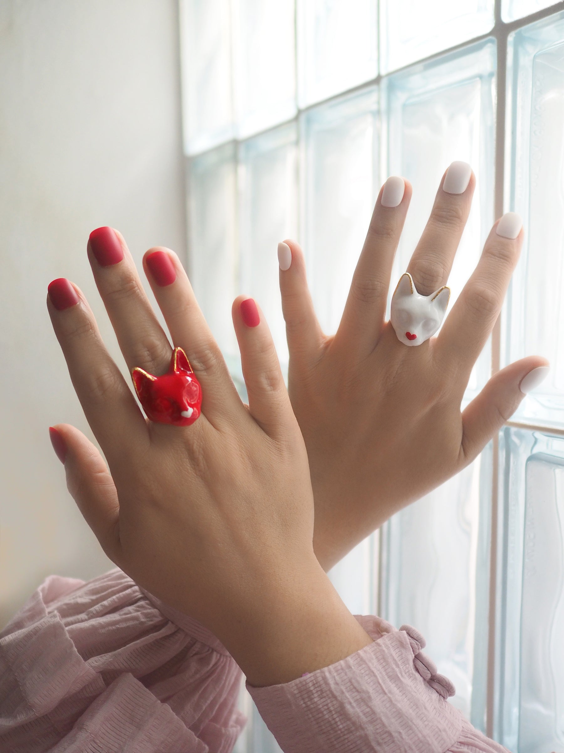 Two hands with stylish rings shaped like a red cat and a white cat