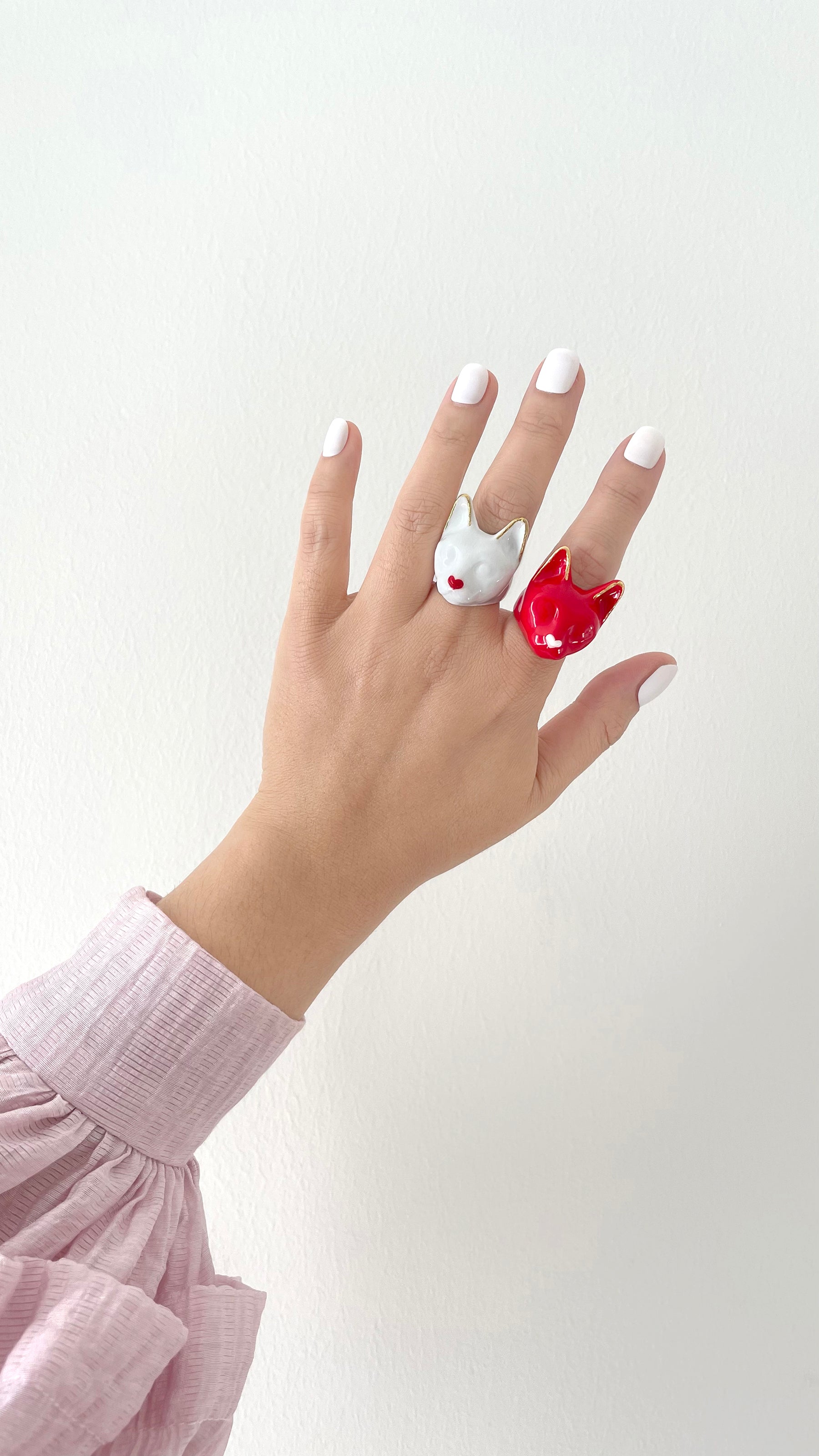 A hand adorned with two cat rings, one white with a small red heart other red with a small white heart.