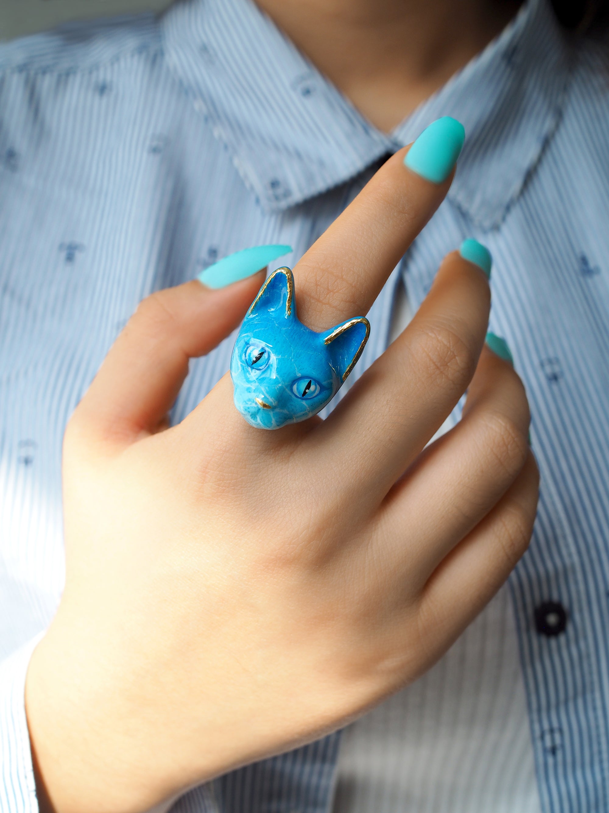 A hand with blue-colored nails is displaying a blue cat ring with water-like texture.