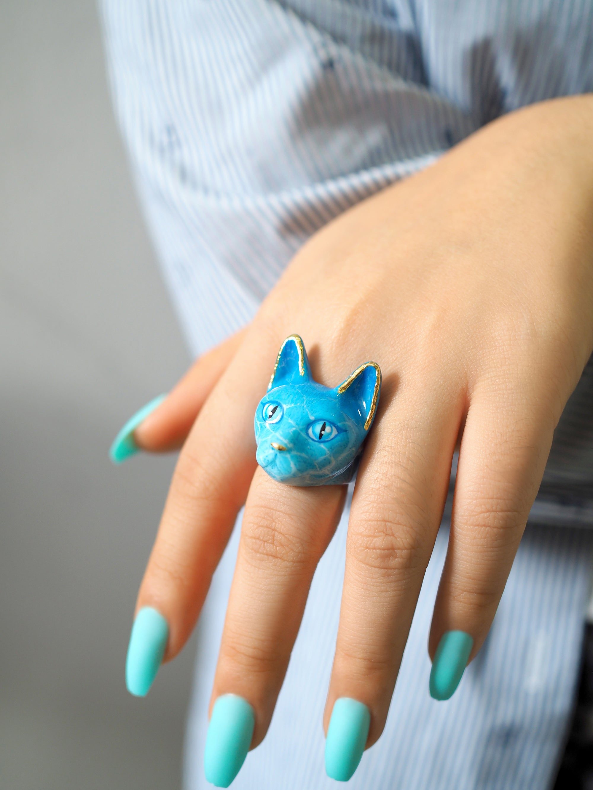 Close-up of a hand wearing a blue cat ring with water-like pattern.