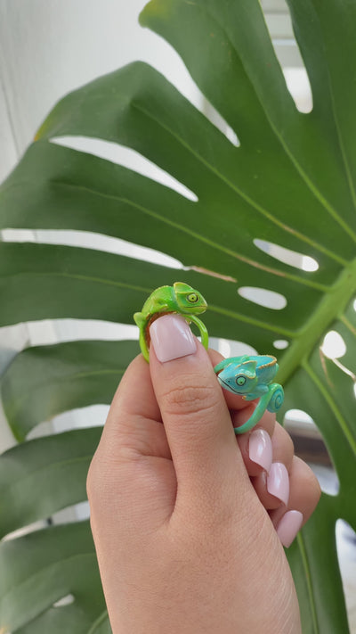 Handmade chameleon rings with playful design displayed on a finger surrounded by greenery.