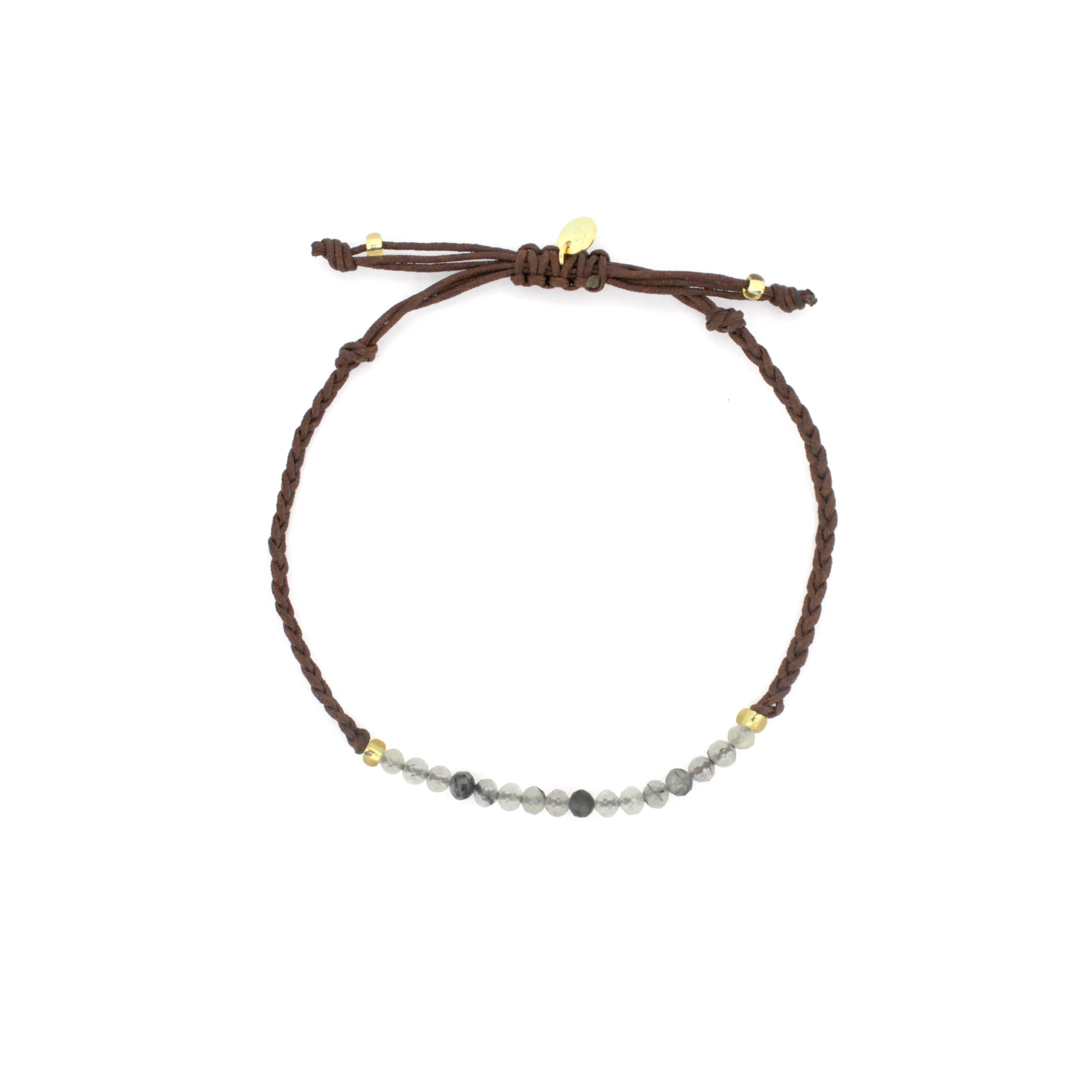 A handcrafted bracelet features a series of grey and white beads with a simple woven brown band.