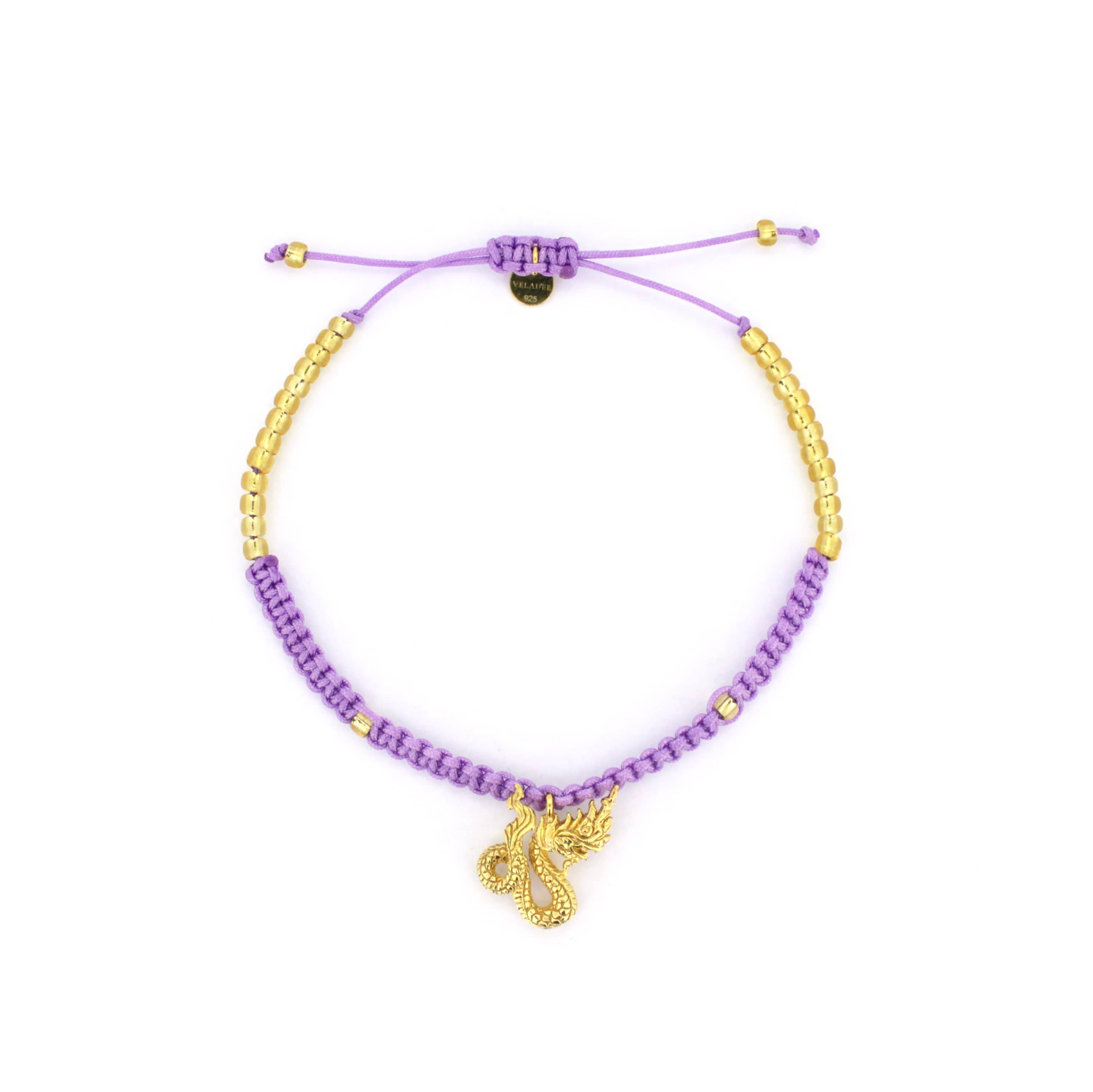 A bracelet featuring a purple woven design material adorned with a gold Naga charm. 