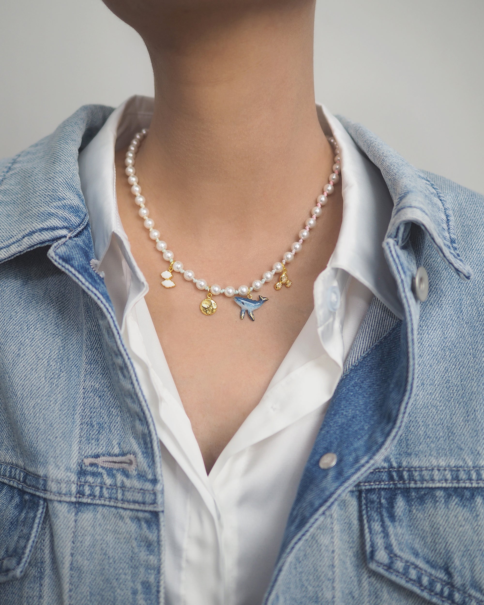 Close-up of a charming pearl choker featuring whimsical charms, worn with a denim jacket.