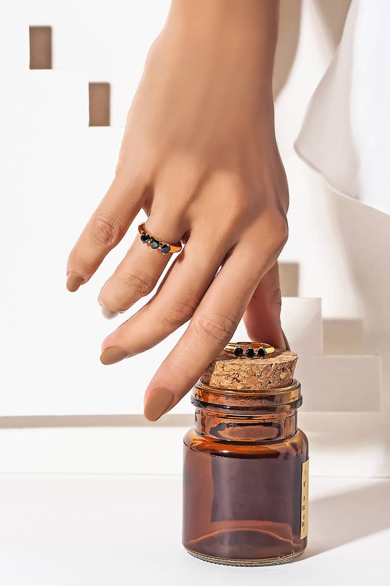 A hand with a black synthetic gemstone ring reaches for a small amber glass jar with a cork lid.