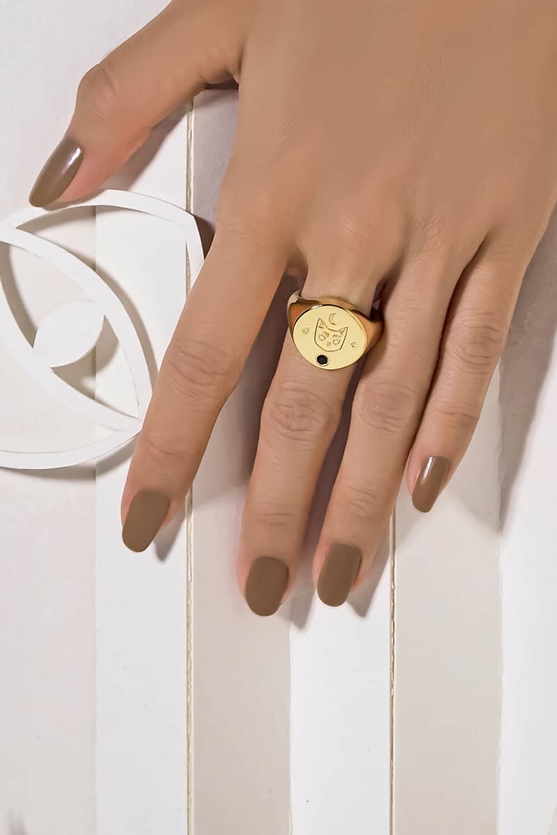 A charming gold signet ring featuring a cat design with a synthetic black gemstone and moon motifs on worn a hand.