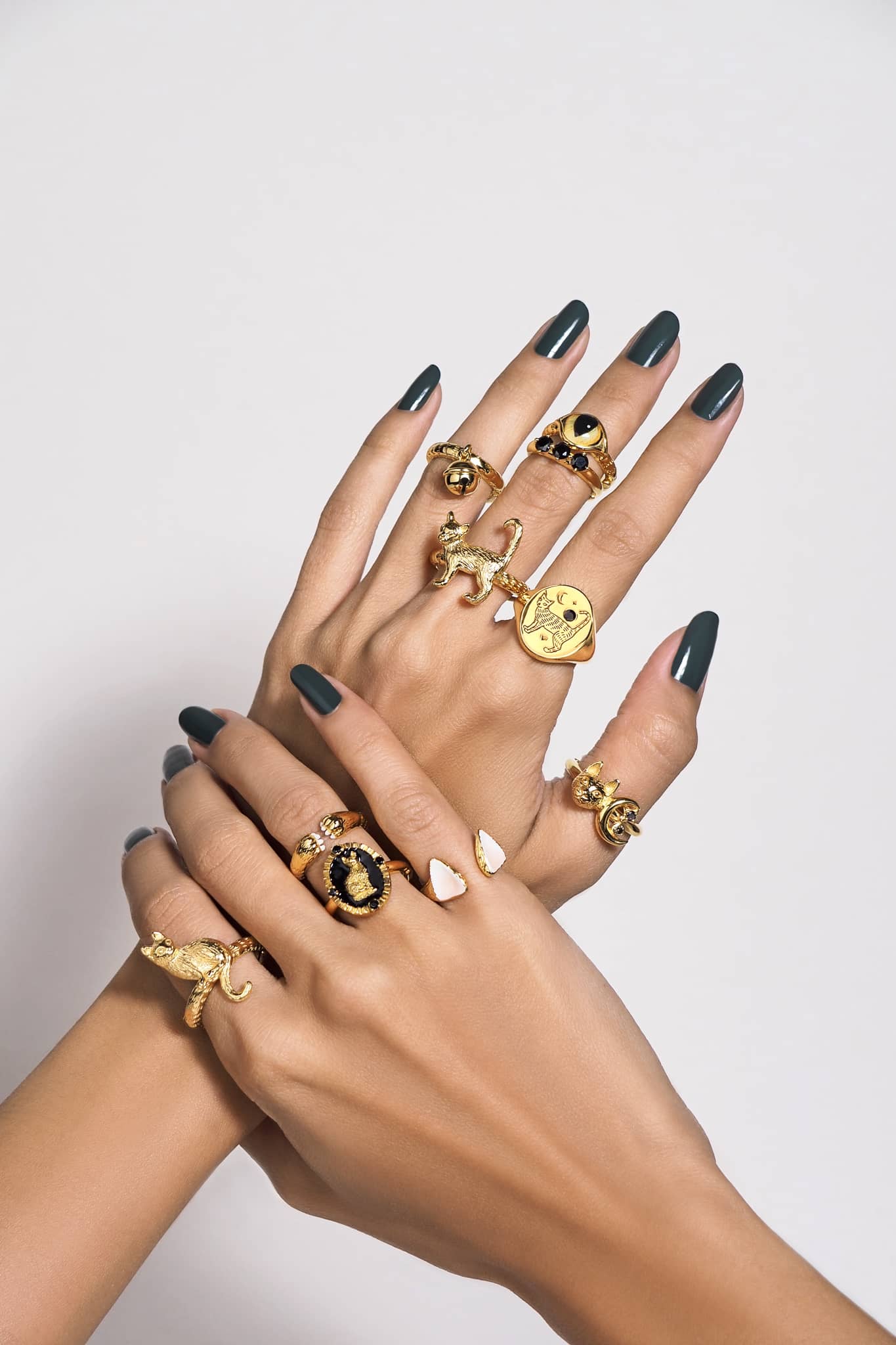 A close-up of two hands overlapping, showcasing multiple gold rings with various designs, including a cat, a moon, and a black stone.