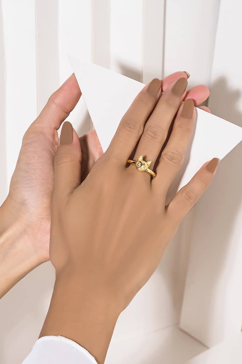 A close-up of a hand wearing gold ring with a cat head design while holding a paper.