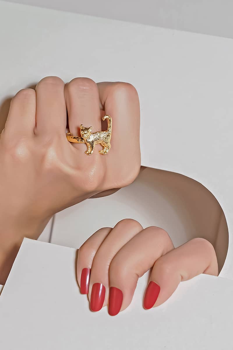 A hand showcasing with a gold ring featuring standing cat design while holding paper.