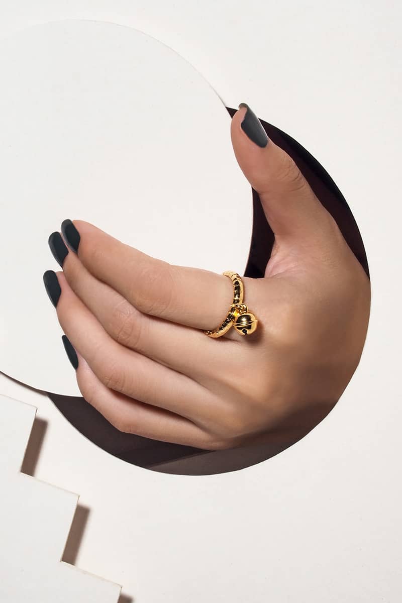 A hand showcasing a gold ring featuring a small cat bell charm. 