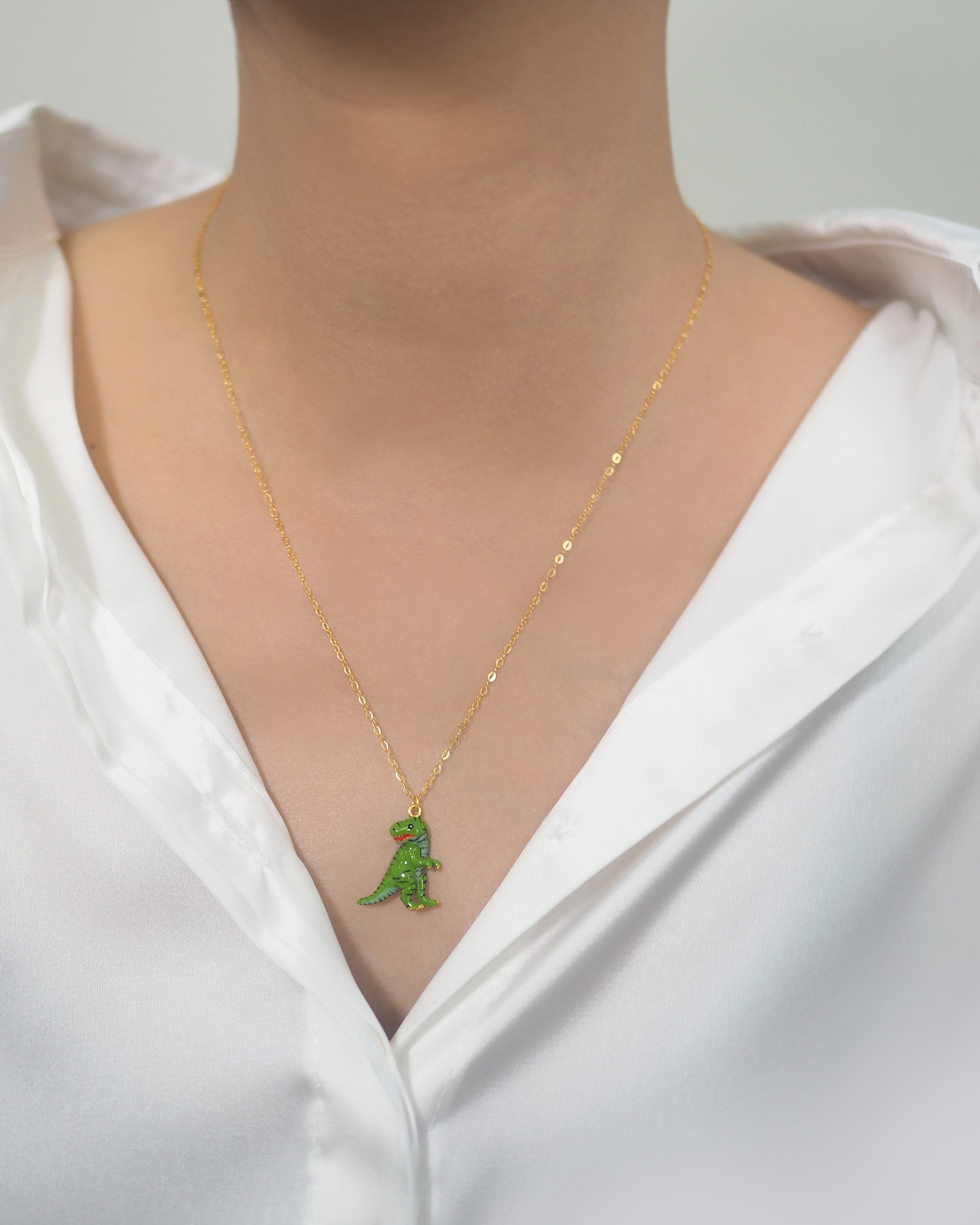 Close-up of a green T-rex charm necklace worn on a person.