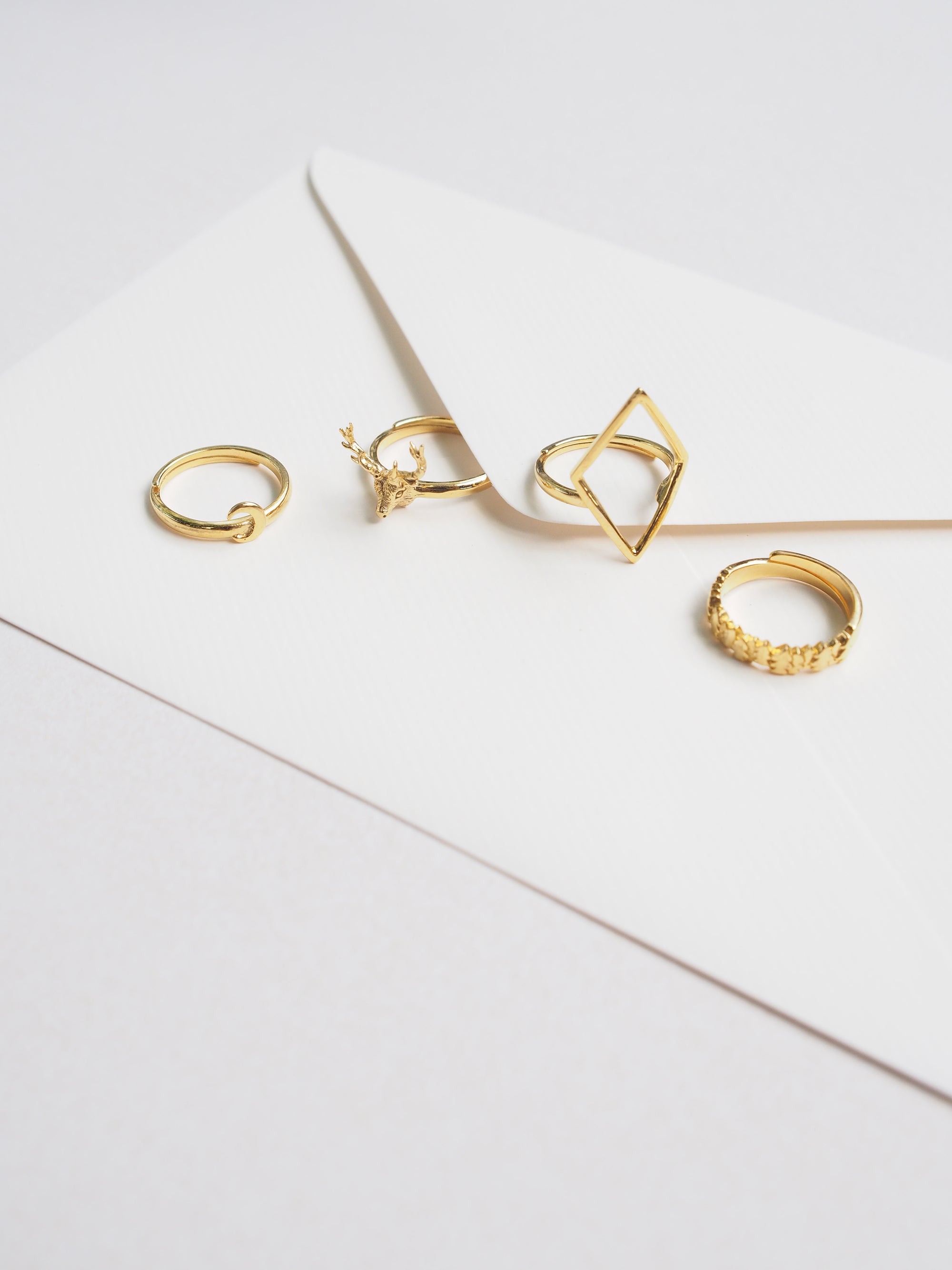 A stunning collection of golden rings featuring unique designs, including the Deer Ring, Forest Ring, Moon Ring, and Rhombus Ring, placed on a letter.