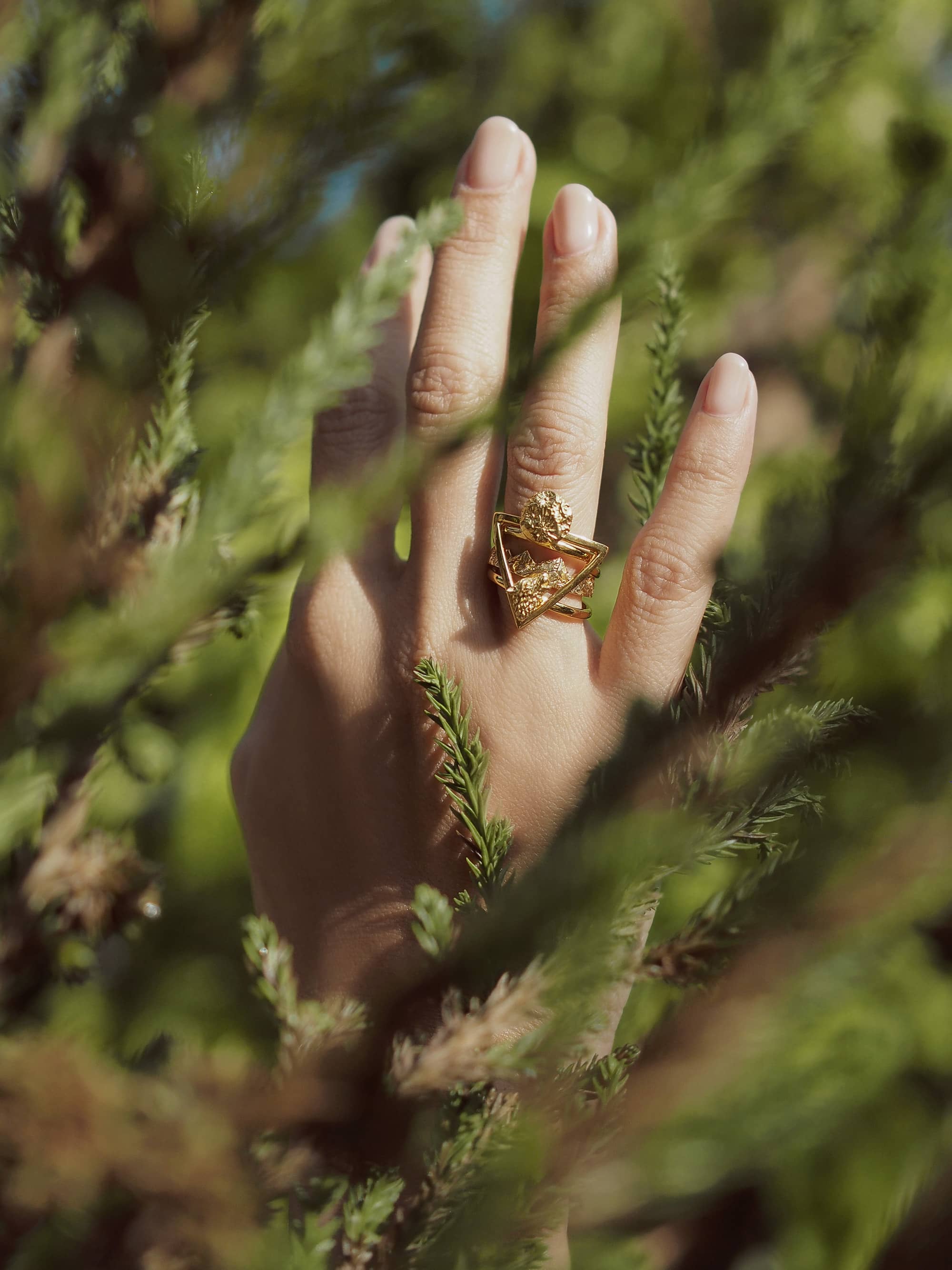 Gold wolf stacking ring set displayed on a hand among greenery.