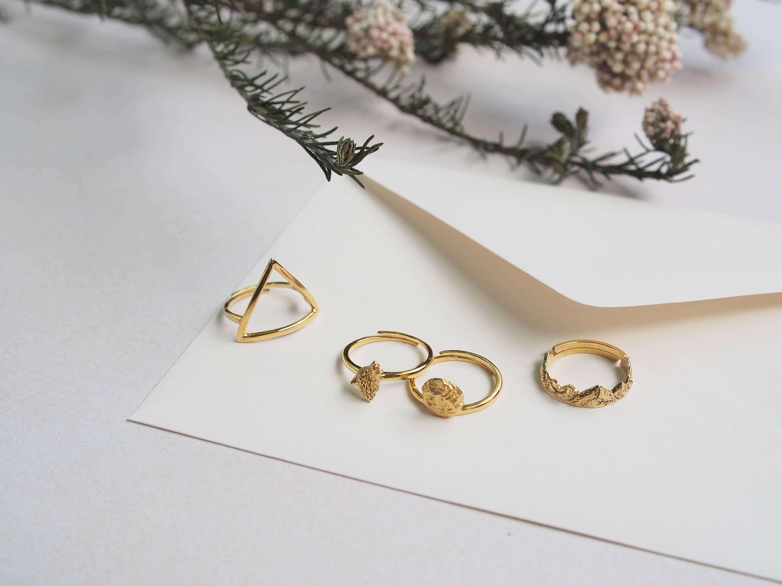 A stunning collection of golden rings featuring unique designs, including the Wolf Ring, Mountain Ring, Moon Ring, and Triangle Ring, placed on a letter.