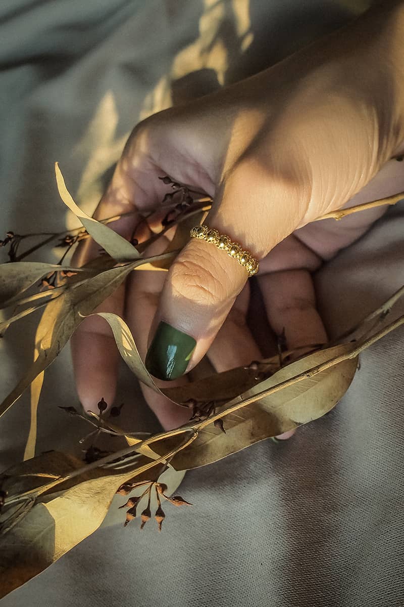 Hand holding dried leaves with a unique gold ring on the finger.