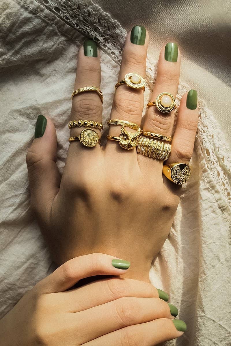 A hand adorned with gold rings featuring an owl and the moon design, inspired by nature, against a soft fabric background.