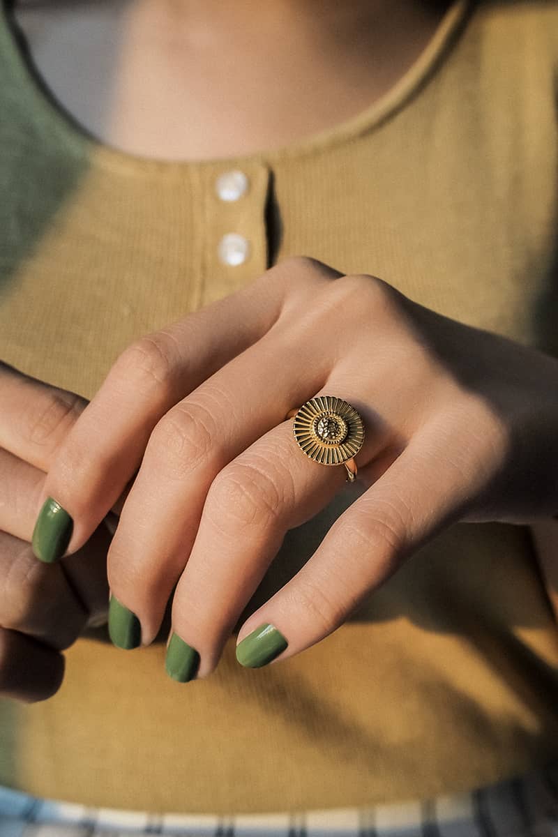 A close-up of a hand with green nail polish adorned with a gold ring with moon design