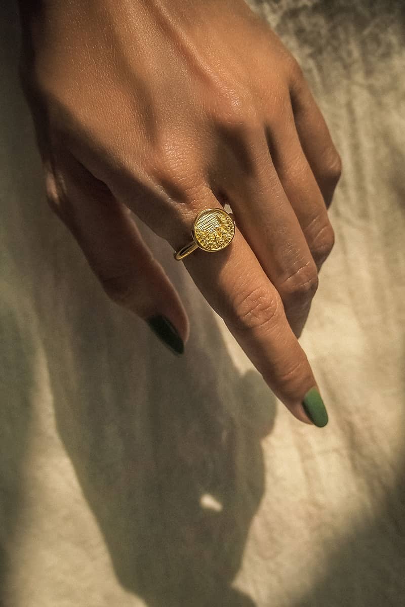 Close up of a hand wearing a gold ring featuring an engraved forest scene