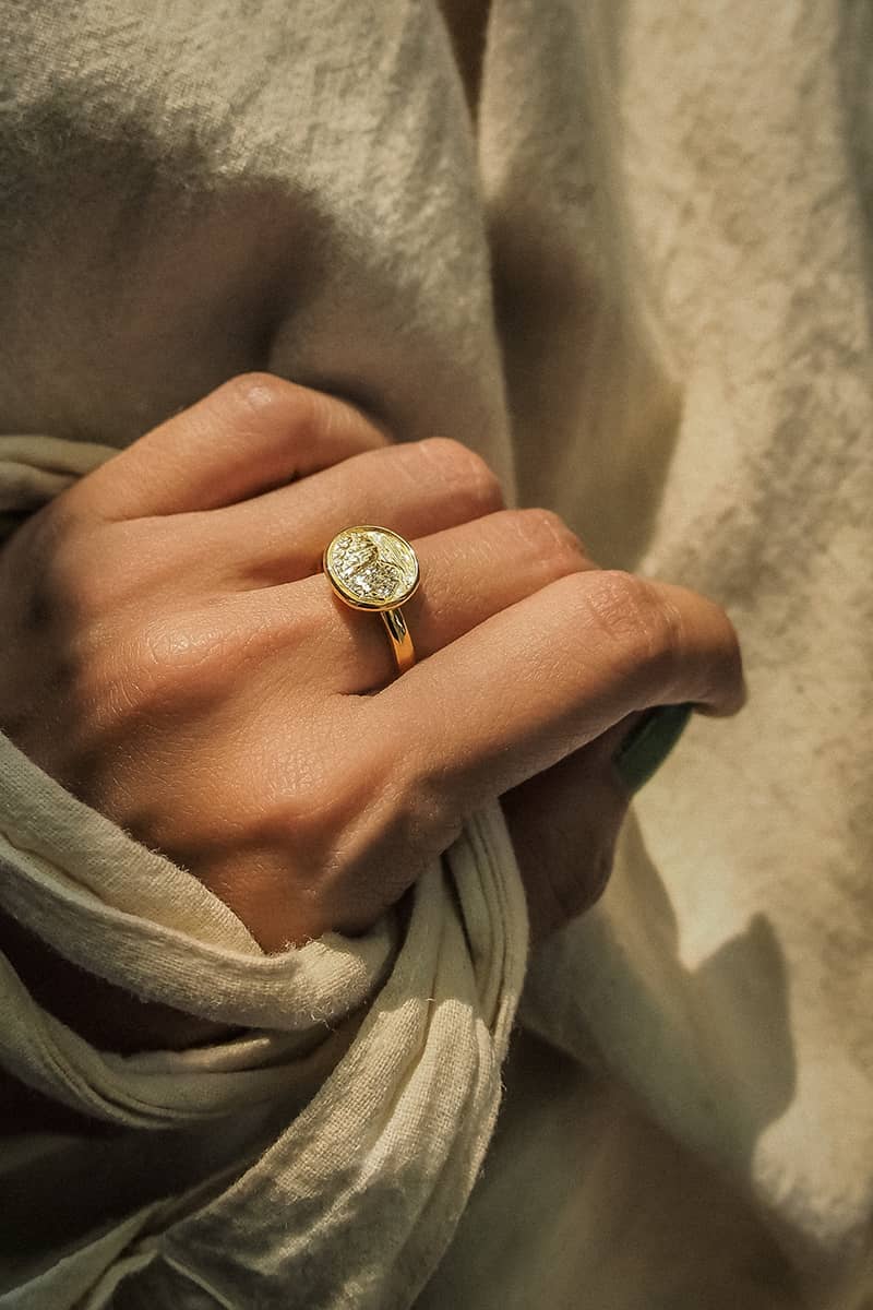 Close up of a hand wearing a gold ring featuring an engraved mountain scene while holding fabric.