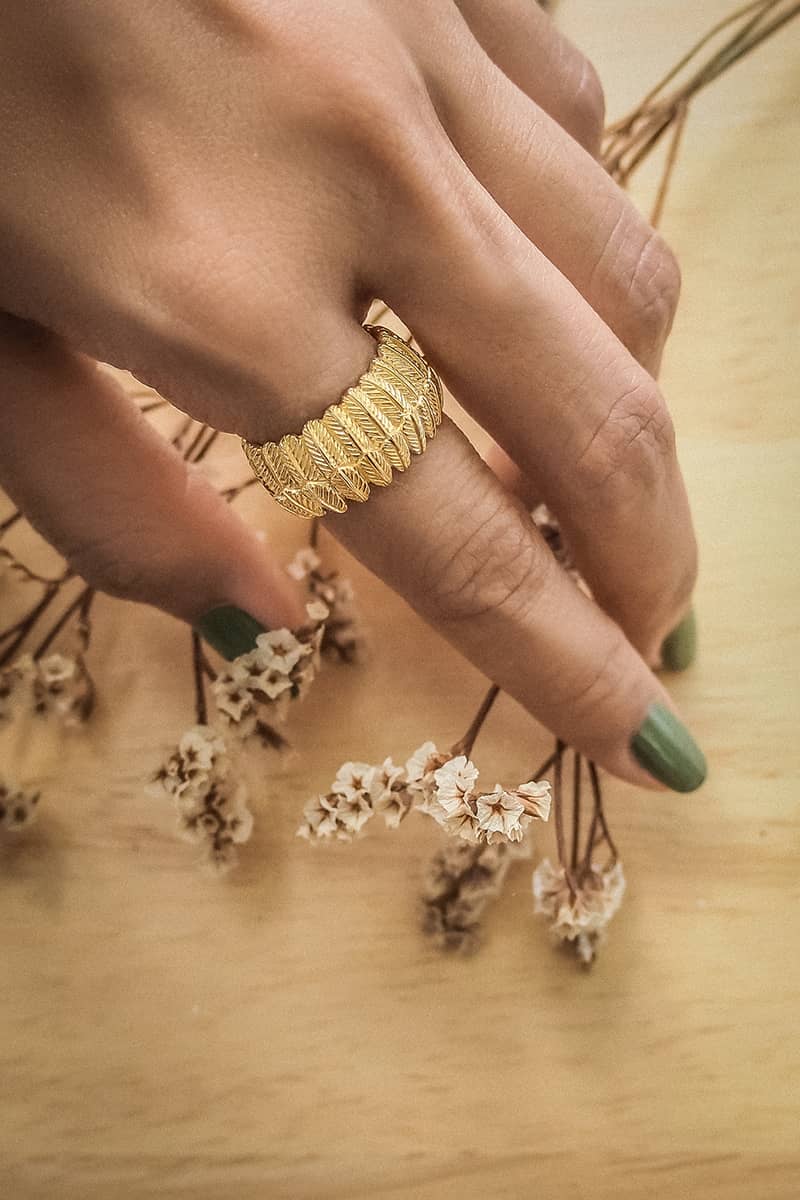 A close-up of a hand wearing a gold ring designed with detailed owl feather motifs.