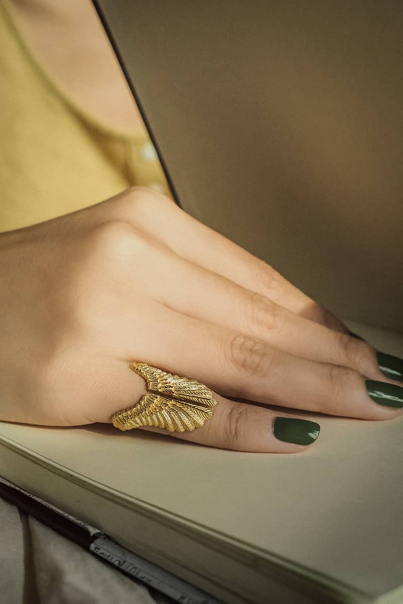 close up of a gold ring designed to resemble owl wings, featuring detailed feather patterns worn on a hand.