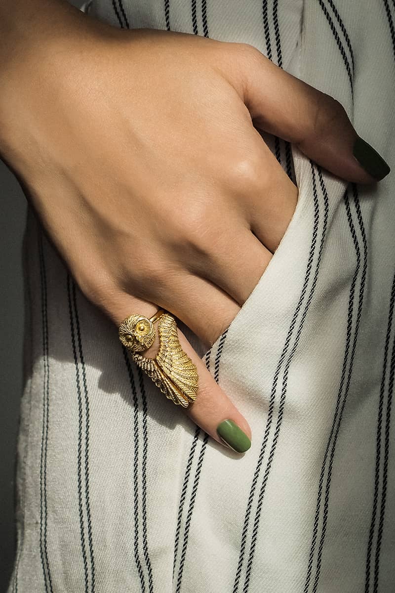 Two unique rings featuring an owl and feather designs, worn on a hand with stylish attire.