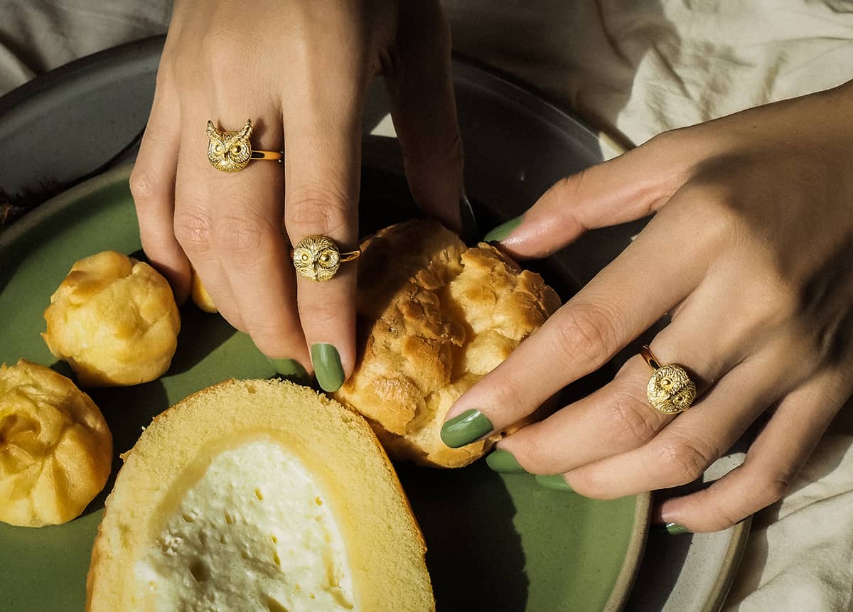 Close-up of hands wearing gold owl rings, holding a piece of bread on a green plate.