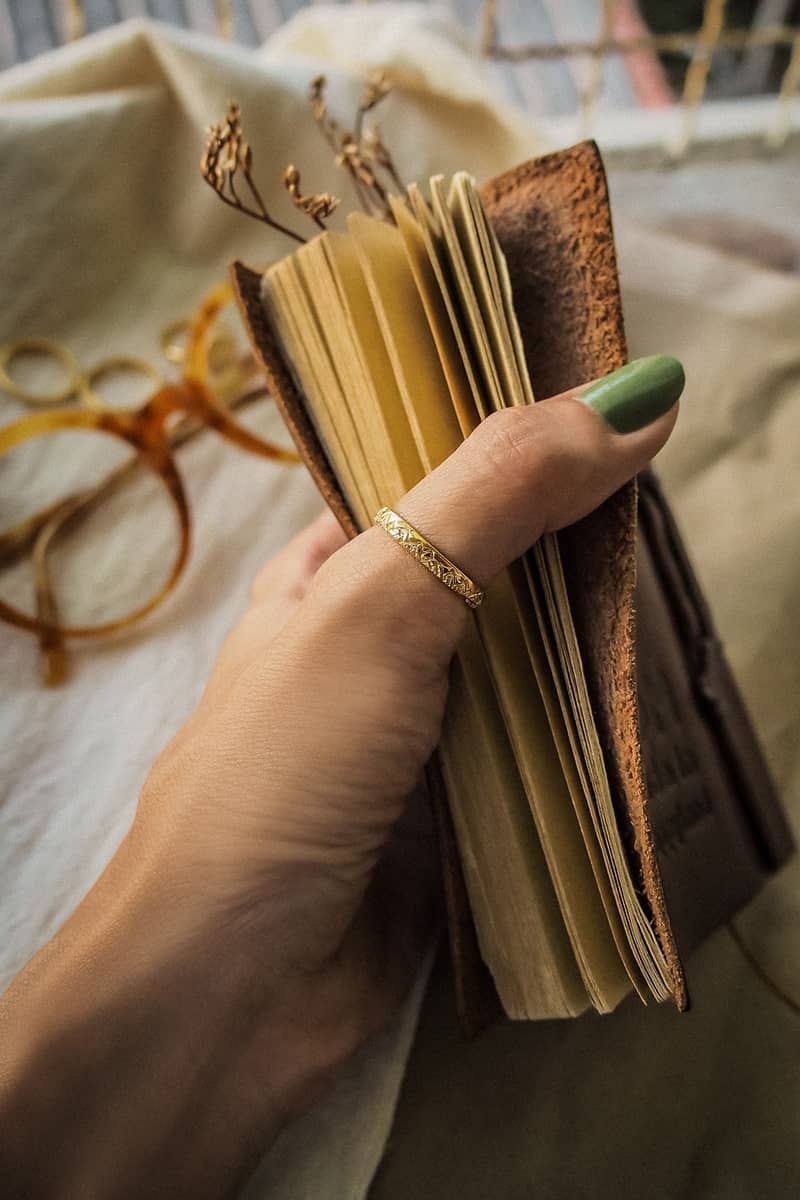 Close-up of a hand adorned with a minimal gold ring featuring mountain patterns holding a vintage book.