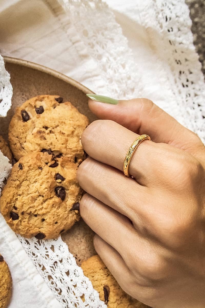 A close-up of a hand with a gold ring with stars pattern placed next to the plate of cookies.