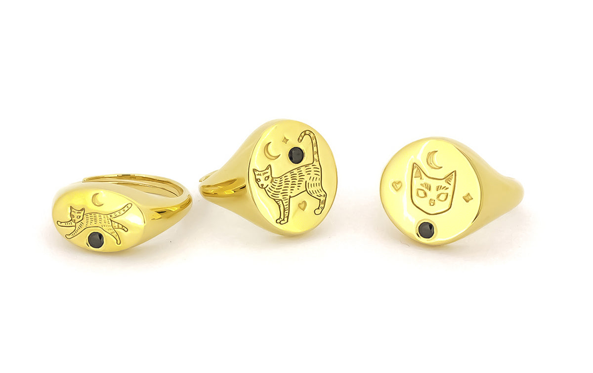 Three gold rings featuring engraved cat designs with black gemstones and moon motifs.