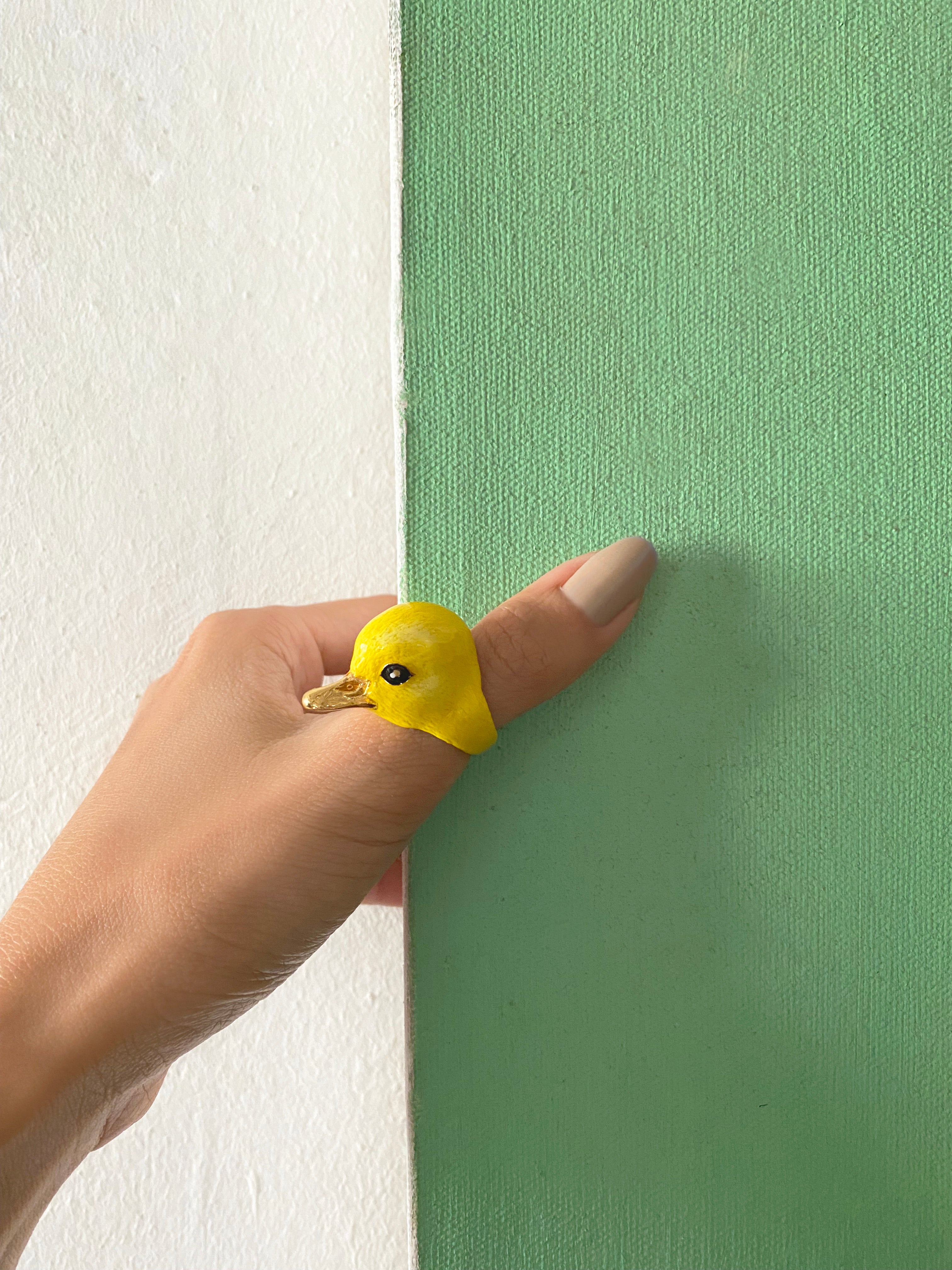 Unique yellow bird ring showcased on a hand with a green background.