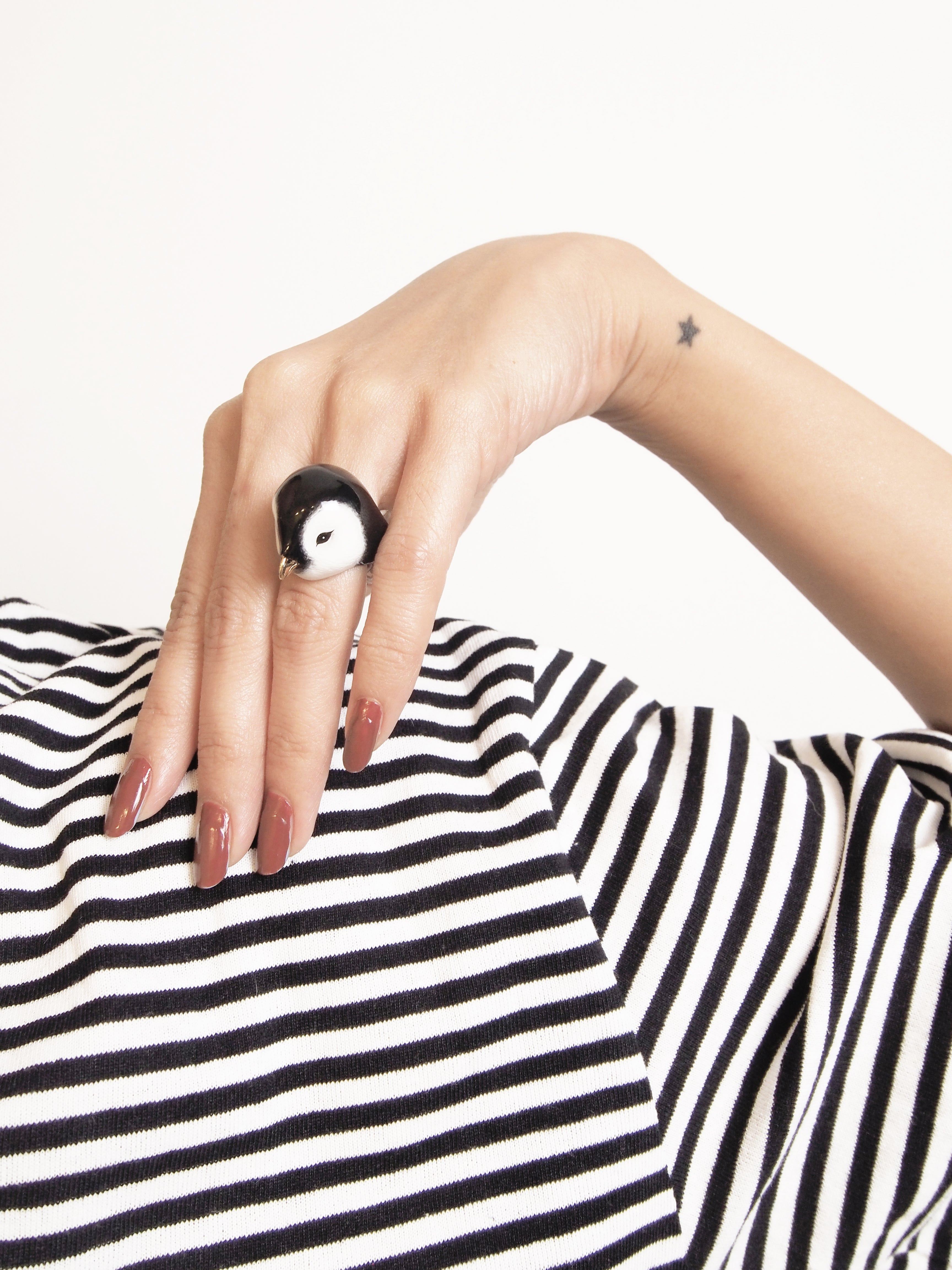 Artistic design of a penguin ring displayed on a woman's hand with a striped shirt.