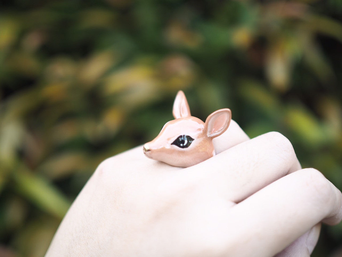 A handcrafted deer ring displayed on a person's hand with greenery in the background.