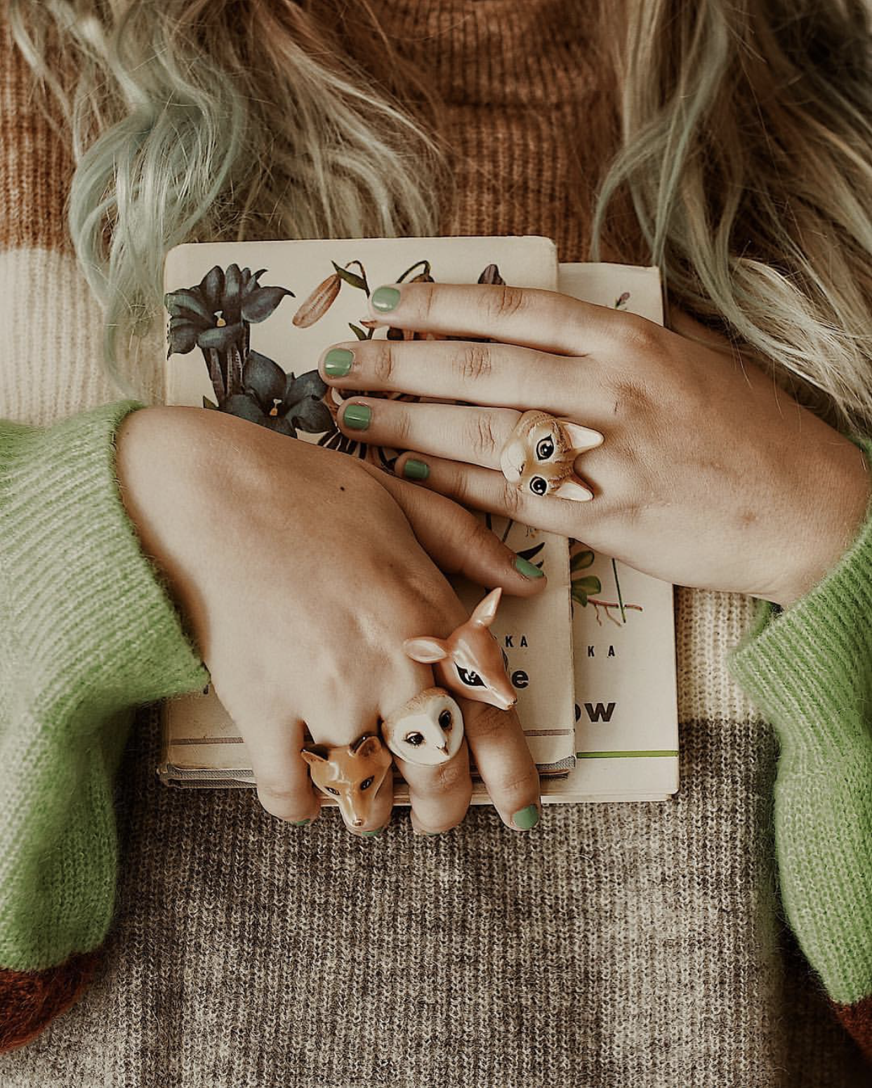 A person's hands wearing three animal rings featuring a deer, fox, owl, and cat.