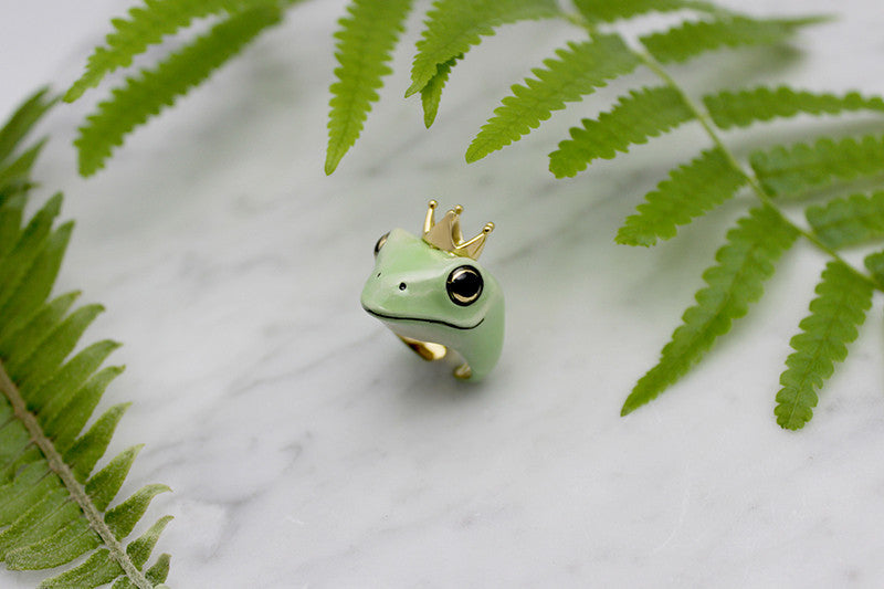 Close-up of a green frog ring with a crown, set on a marble background.