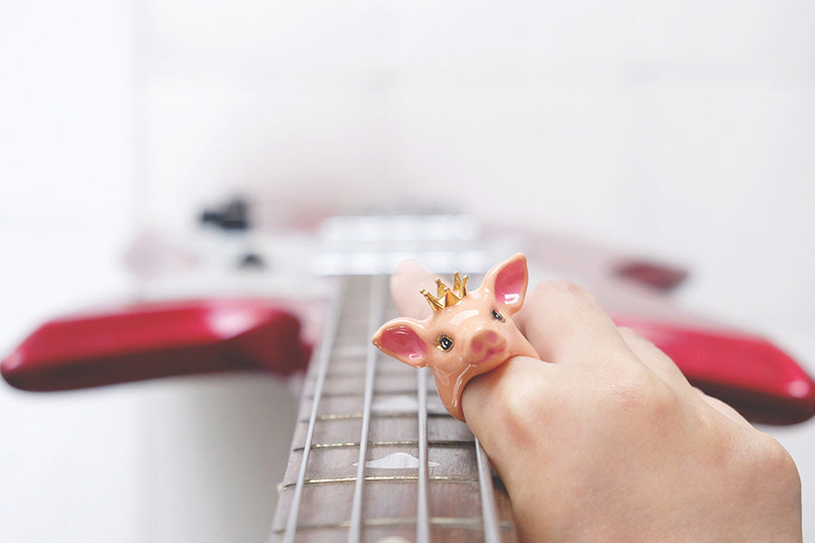 Close-up of a hand adored with a prince pig ring while holding a red bass guitar.