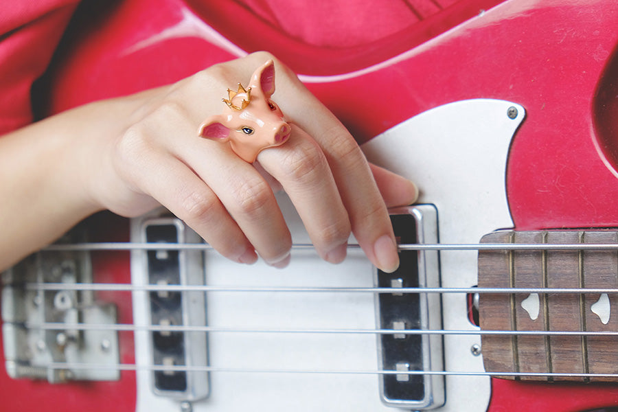 Close-up of a hand adored with a pig ring with golden crown while playing a red bass guitar.