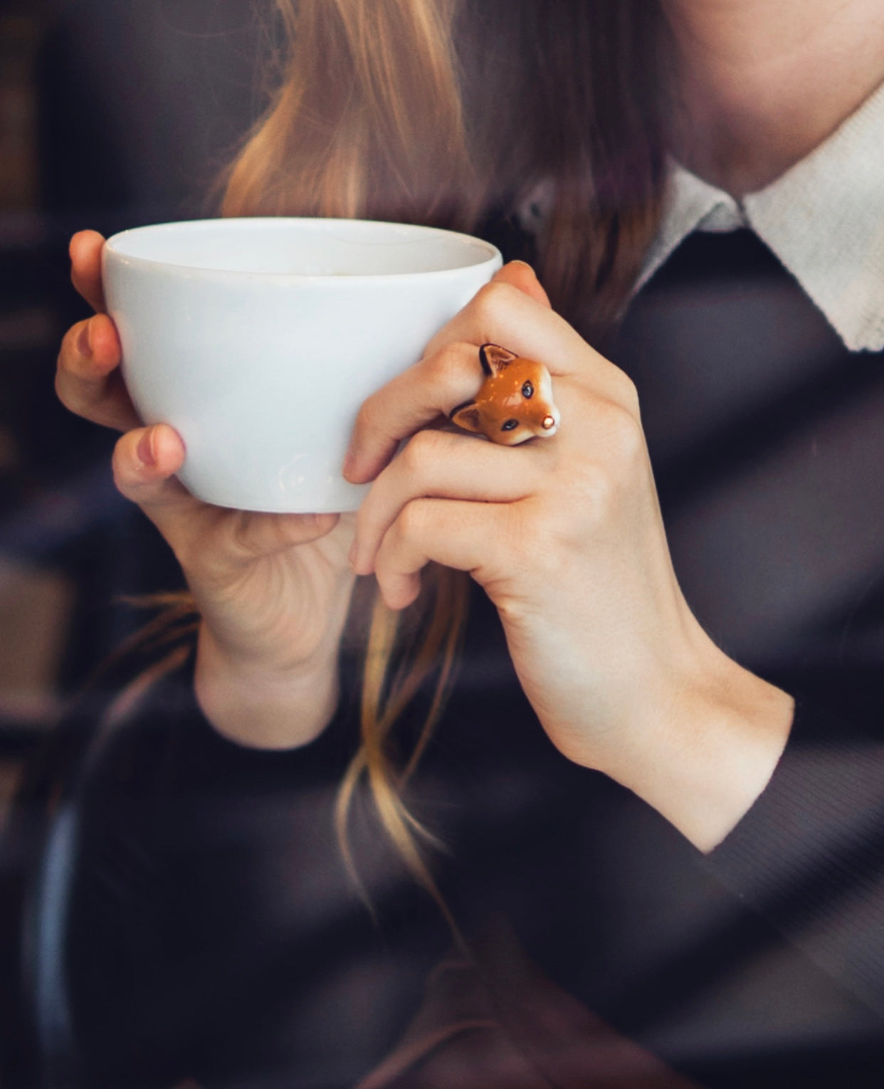 A hand with red fox ring holds a cup of coffee