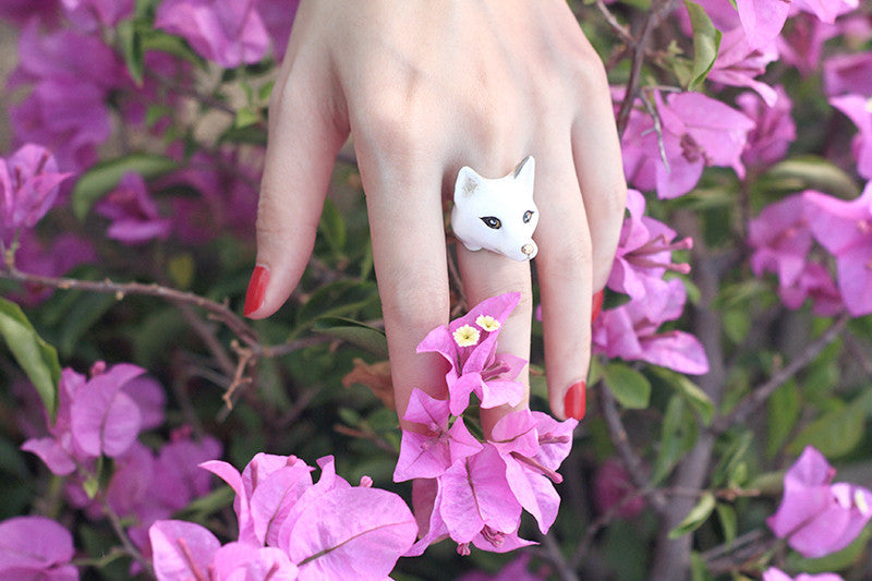 Close-up of a hand wearing a snow fox surrounded by vibrant flowers.